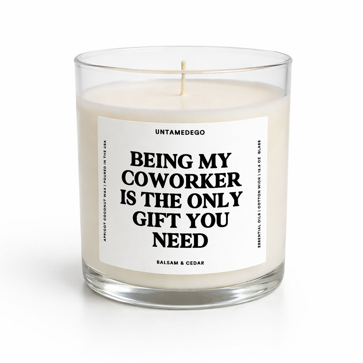 A clear glass jar candle with white wax and a single wick, featuring a white label with bold black text that reads 'BEING MY COWORKER IS THE ONLY GIFT YOU NEED.' The brand name 'UNTAMEDEGO' is visible at the top of the label.