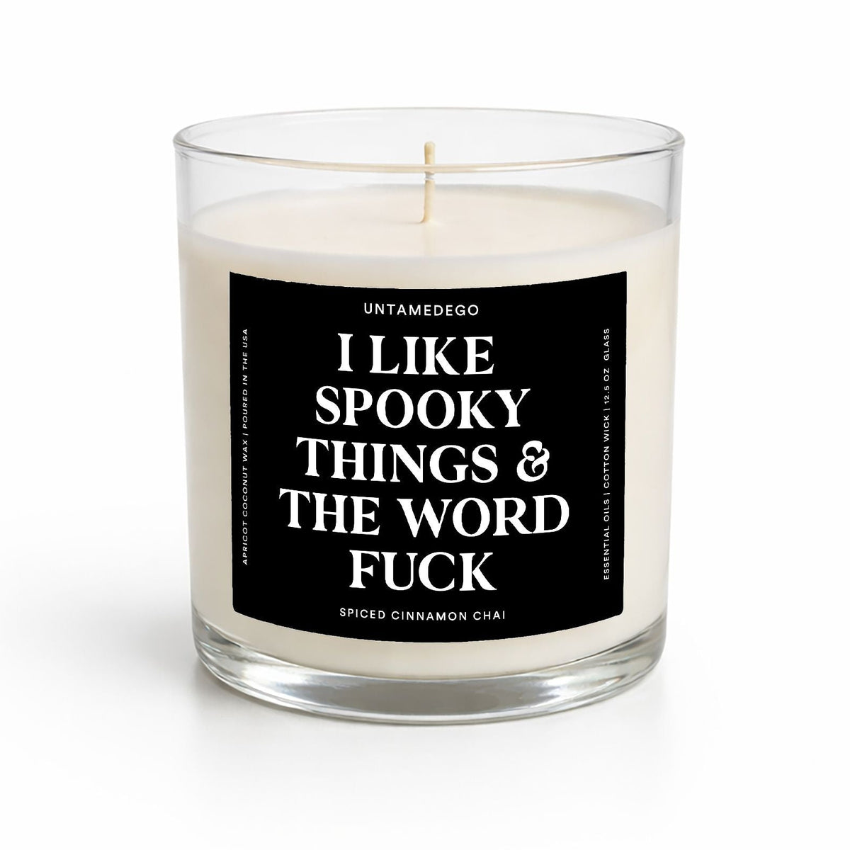 A clear glass jar candle with white wax and a black label featuring bold white text that reads, 'I LIKE SPOOKY THINGS & THE WORD FUCK.' The brand name 'UNTAMEDEGO' is visible at the top of the label, with 'PUMPKIN SPICE' at the bottom.