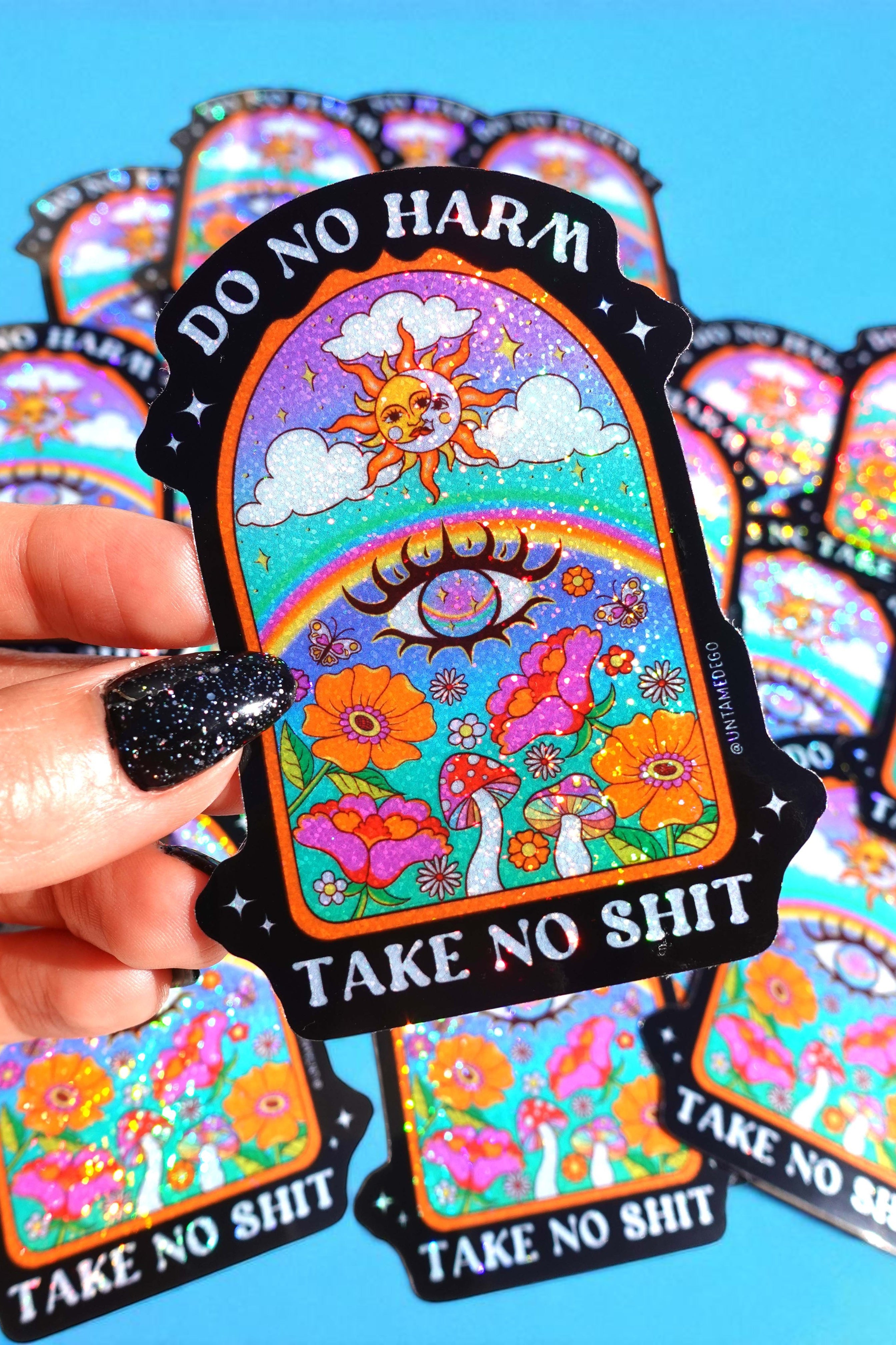 Colorful stickers with 'Do No Harm, Take No Shit' text held by a hand against a blue background.
