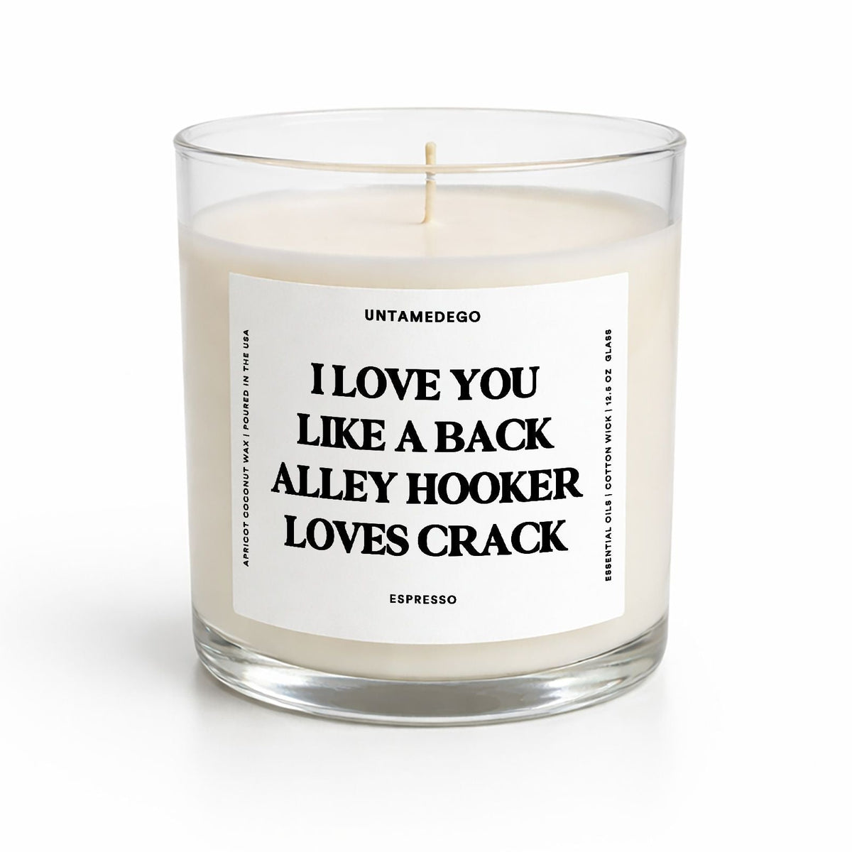 A clear glass jar candle with cream-colored wax and a white label featuring bold black text that reads 'I LOVE YOU LIKE A BACK ALLEY HOOKER LOVES CRACK' by UNTAMEDEGO. The candle is photographed on a clean white background with a soft shadow.