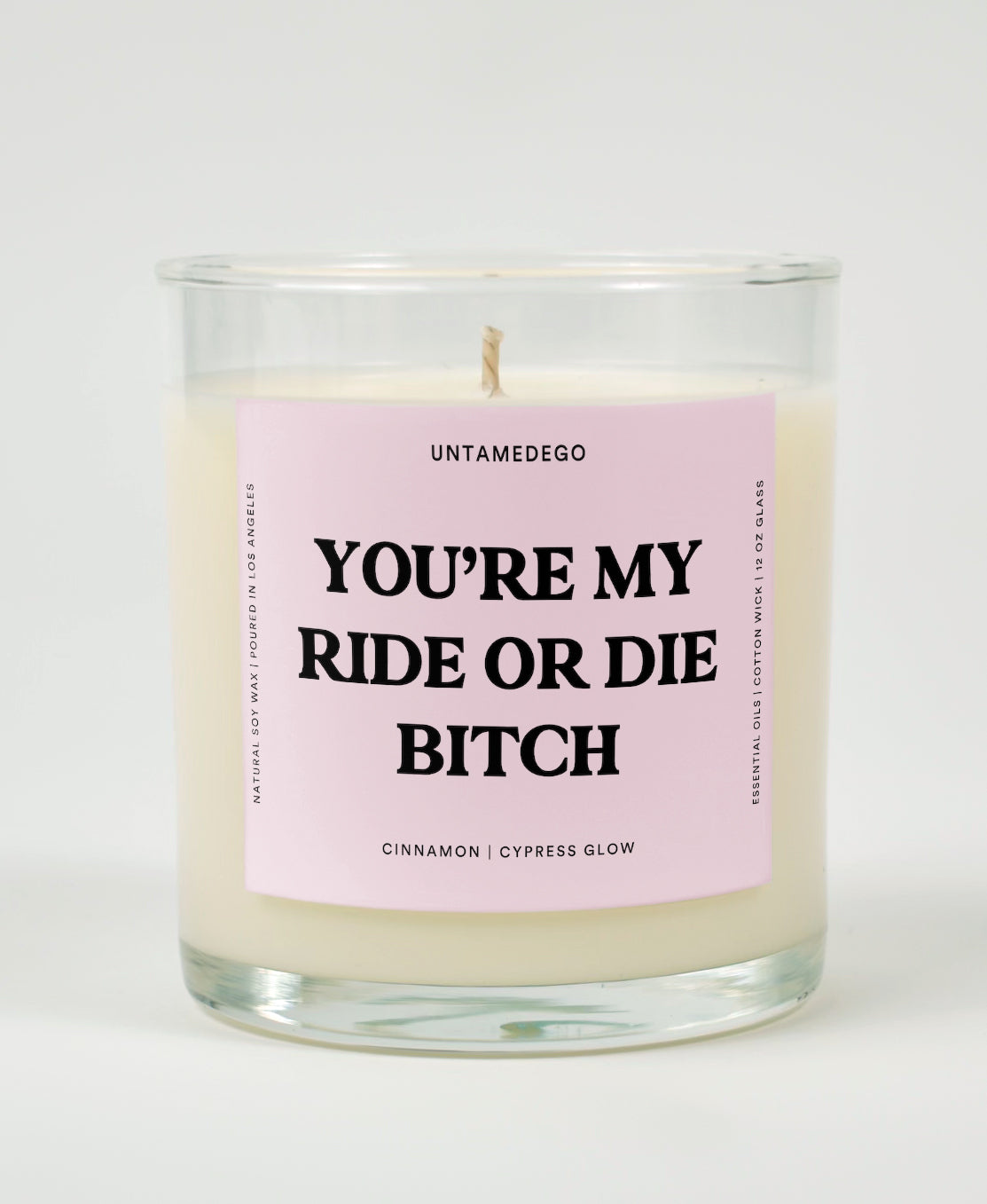 A clear glass candle with a pink label that reads 'YOU'RE MY RIDE OR DIE BITCH' on the front, with additional text indicating the fragrance.