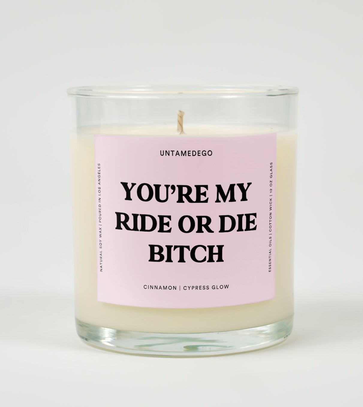 A clear glass candle with a pink label that reads 'YOU'RE MY RIDE OR DIE BITCH' on the front, with additional text indicating the fragrance.