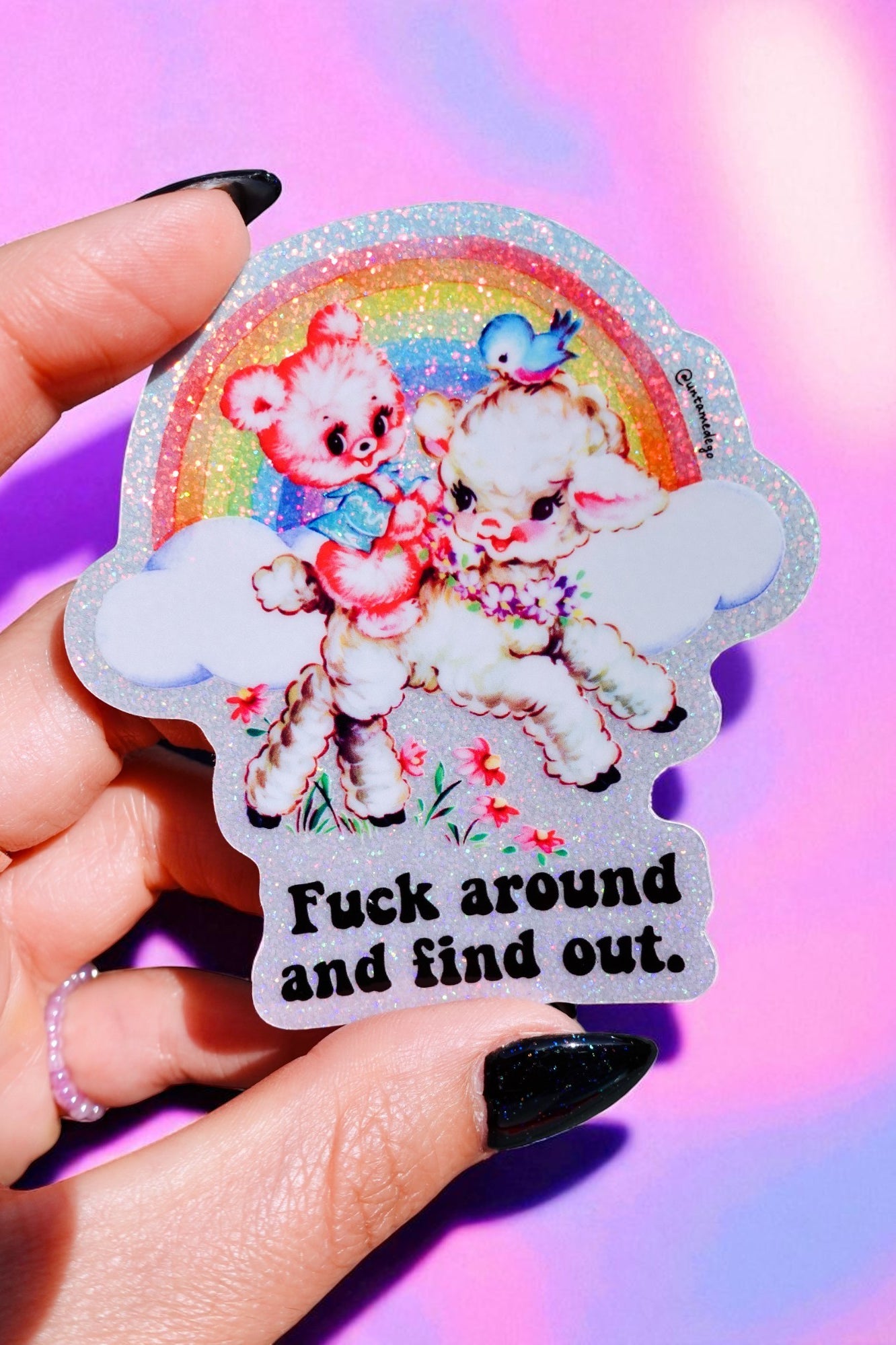 Sticker with cartoon bears and rainbow, held by a hand against a colorful background.