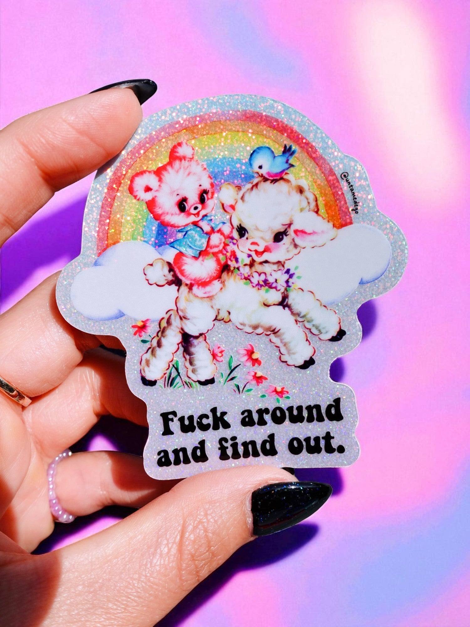 Sticker with cartoon bears and rainbow, held by a hand against a colorful background.