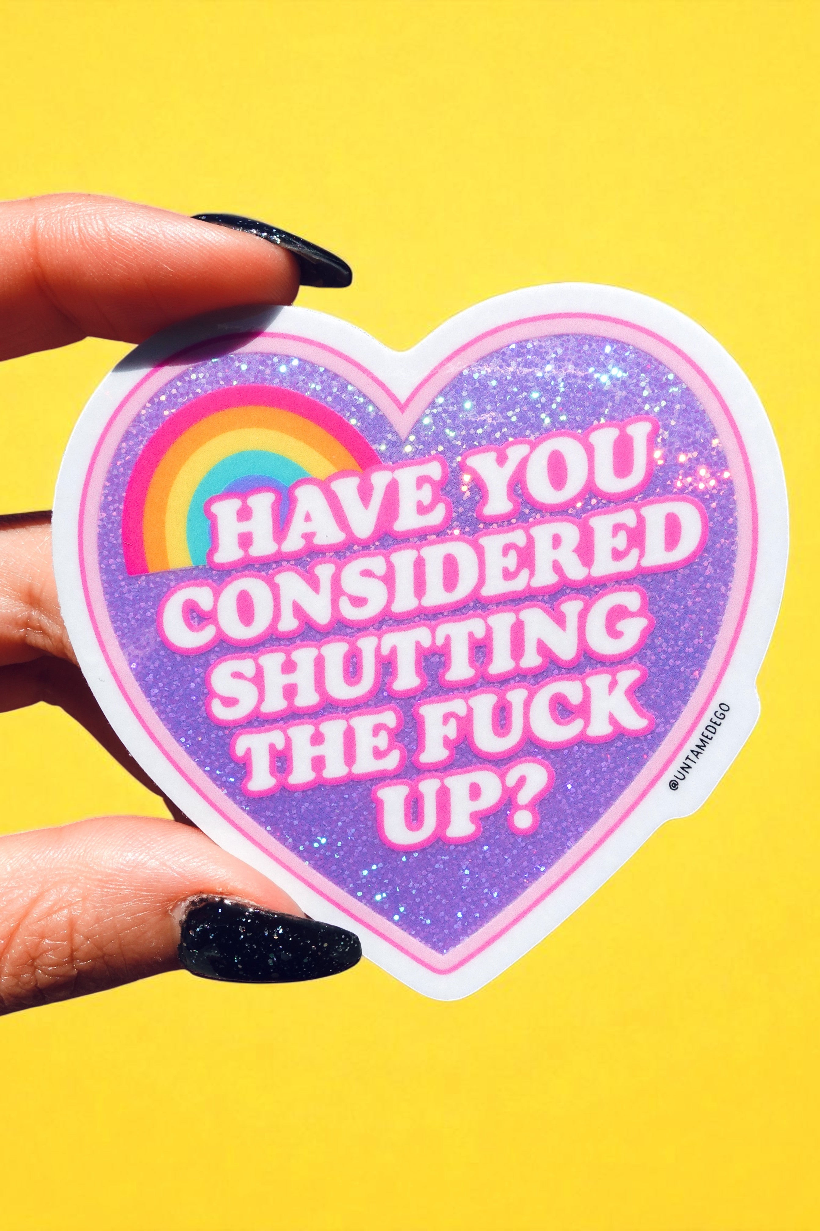 Heart-shaped sticker with colorful text held by a hand against a yellow background