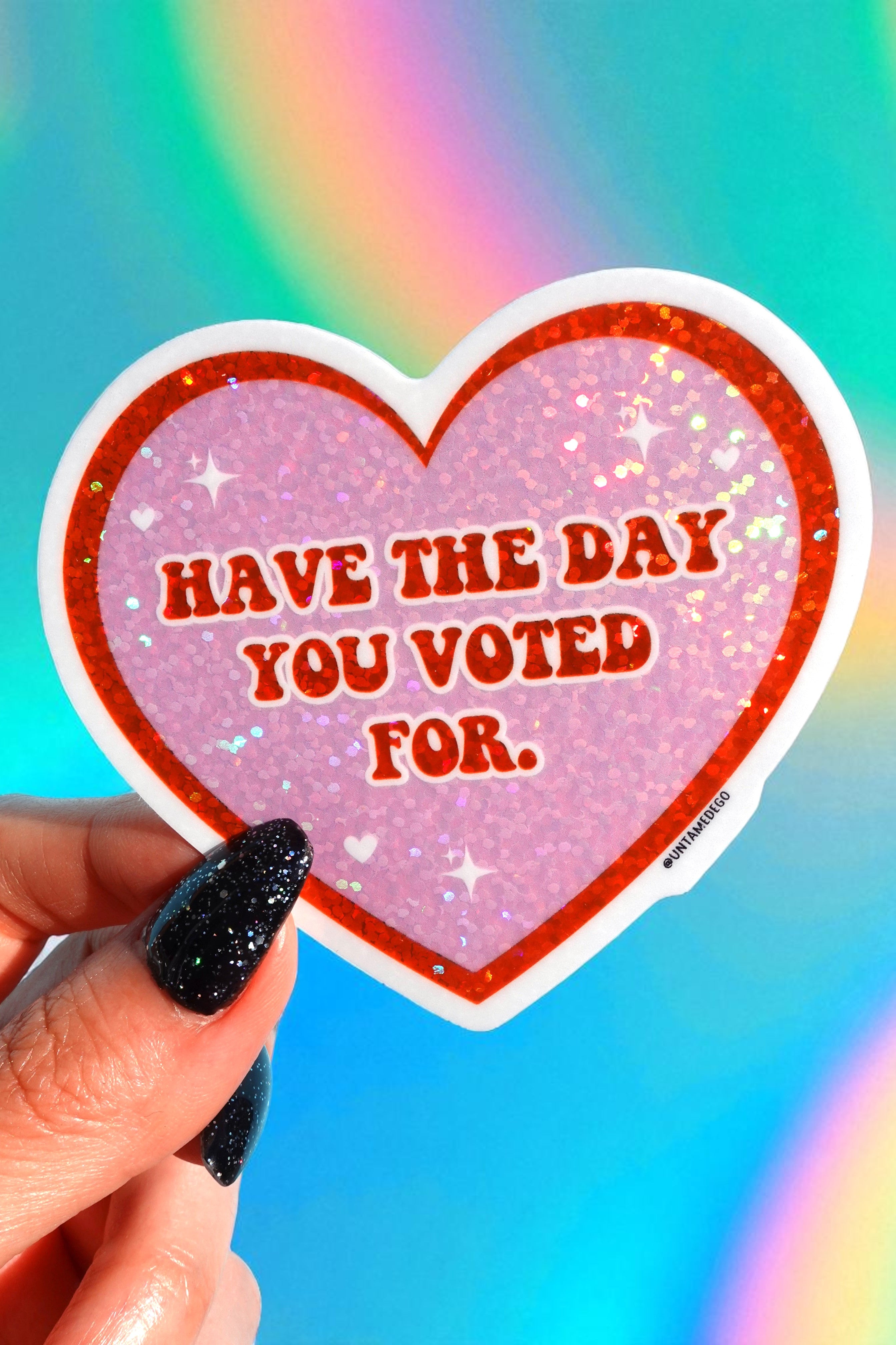 Heart-shaped sticker with 'Have the day you voted for.' text held by a hand against a colorful background