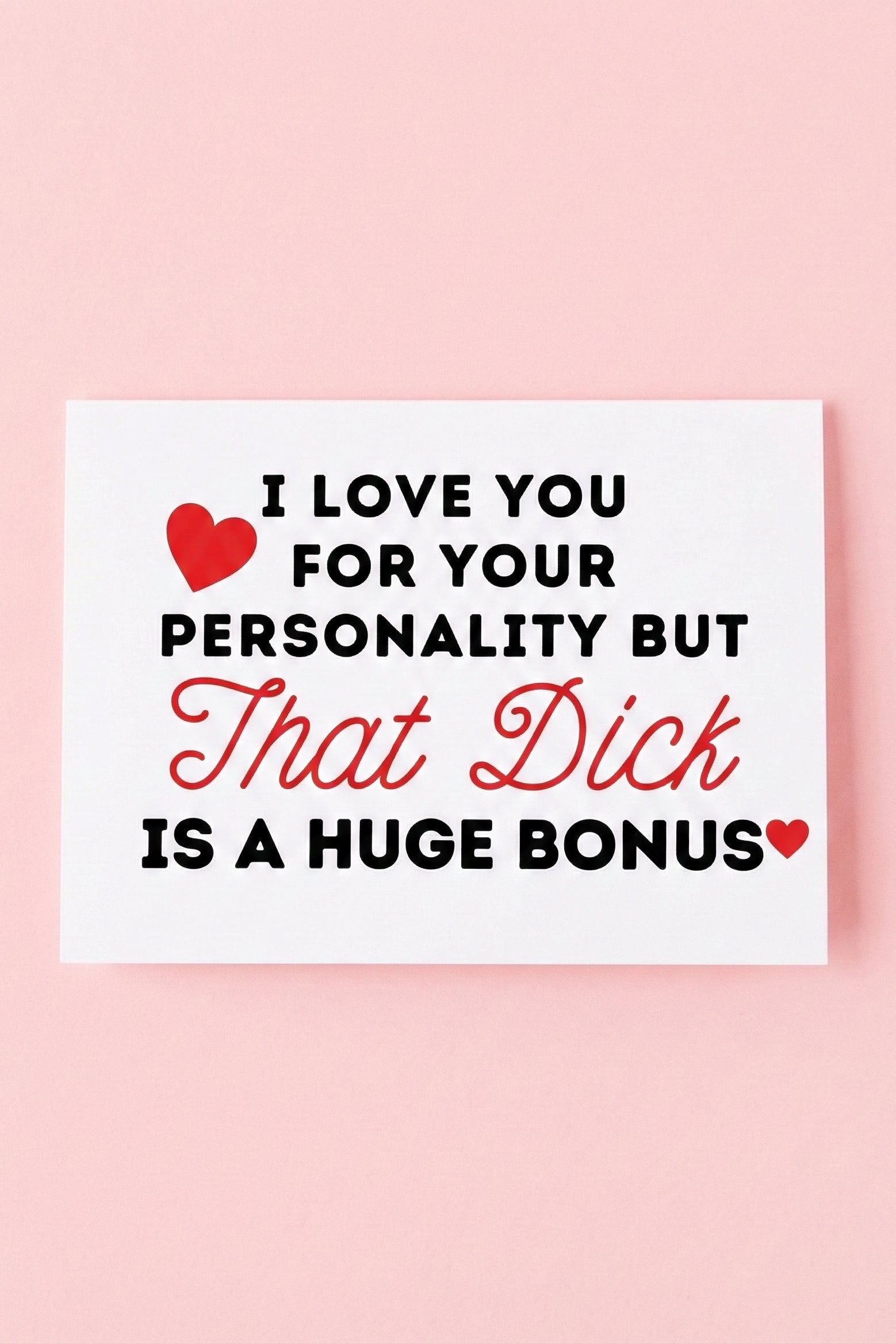 Greeting card displaying a humorous adult phrase in black and red text with heart graphics, photographed against a pink background