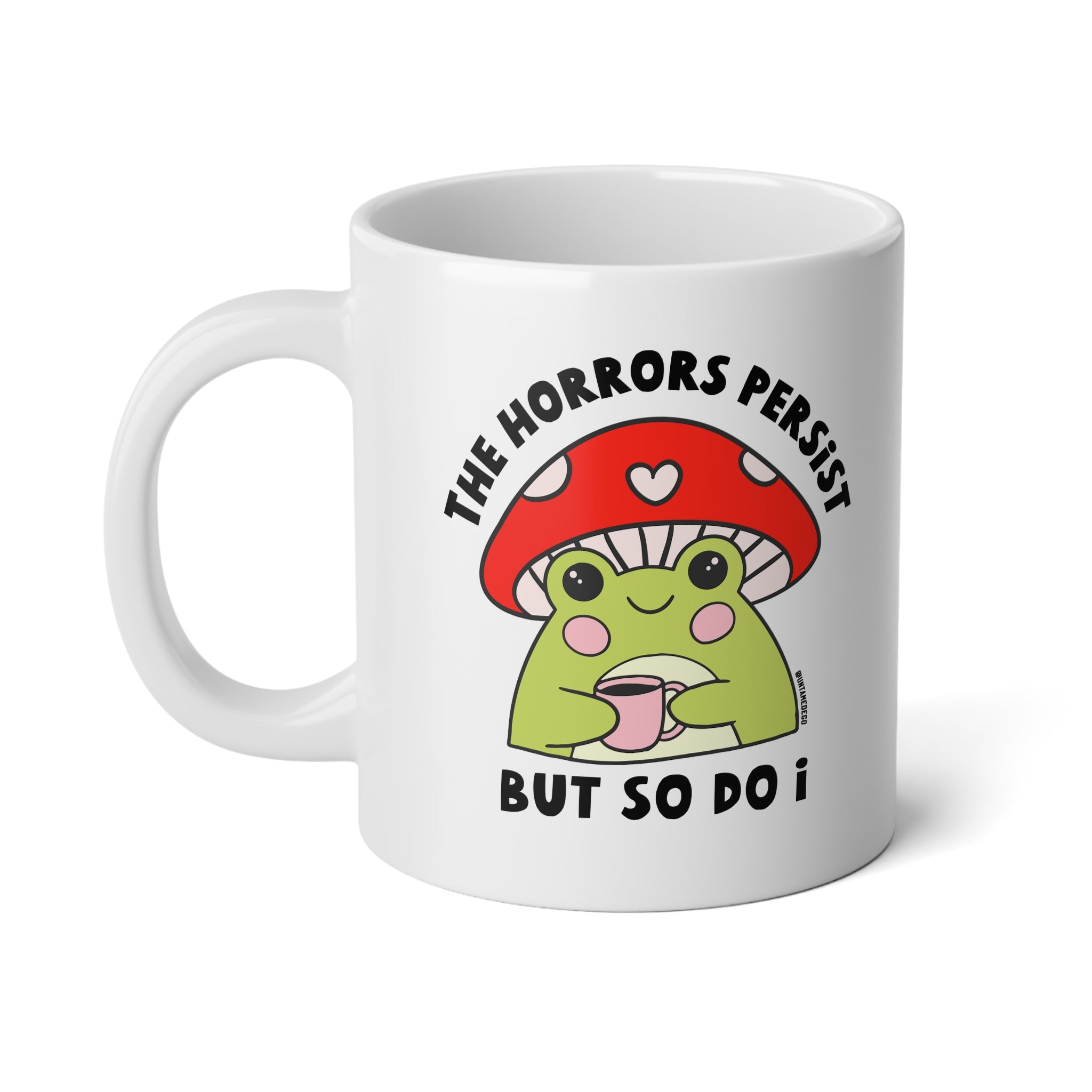 A white ceramic mug featuring a cartoon graphic of a green frog under a red mushroom cap, with the text 'THE HORRORS PERSIST BUT SO DO I' printed in black.