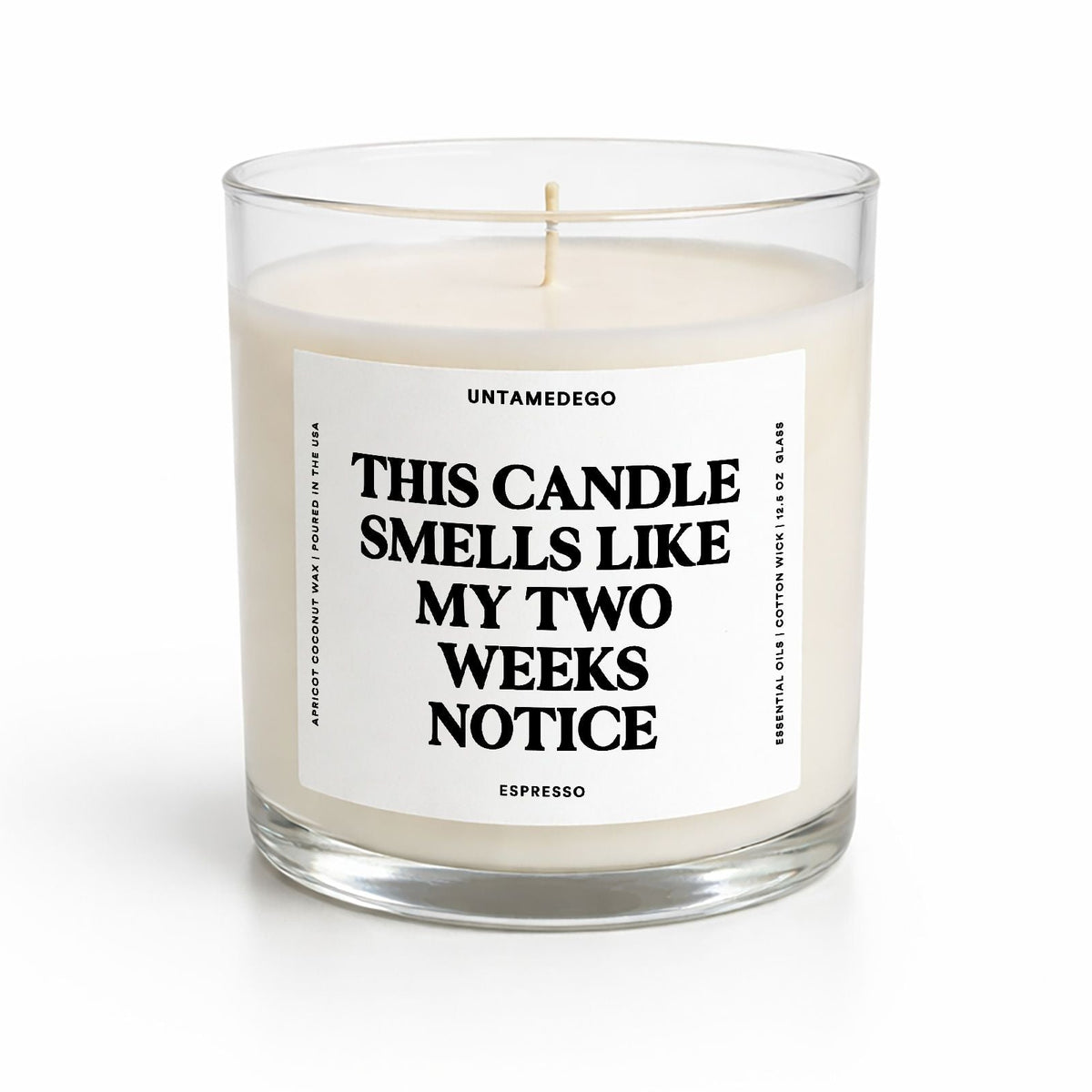 A clear glass jar candle with white wax and a single wick, featuring a white label with bold black text that reads 'THIS CANDLE SMELLS LIKE MY TWO WEEKS NOTICE' and the brand name 'UNTAMEDEGO' above. The candle is photographed on a clean white background.