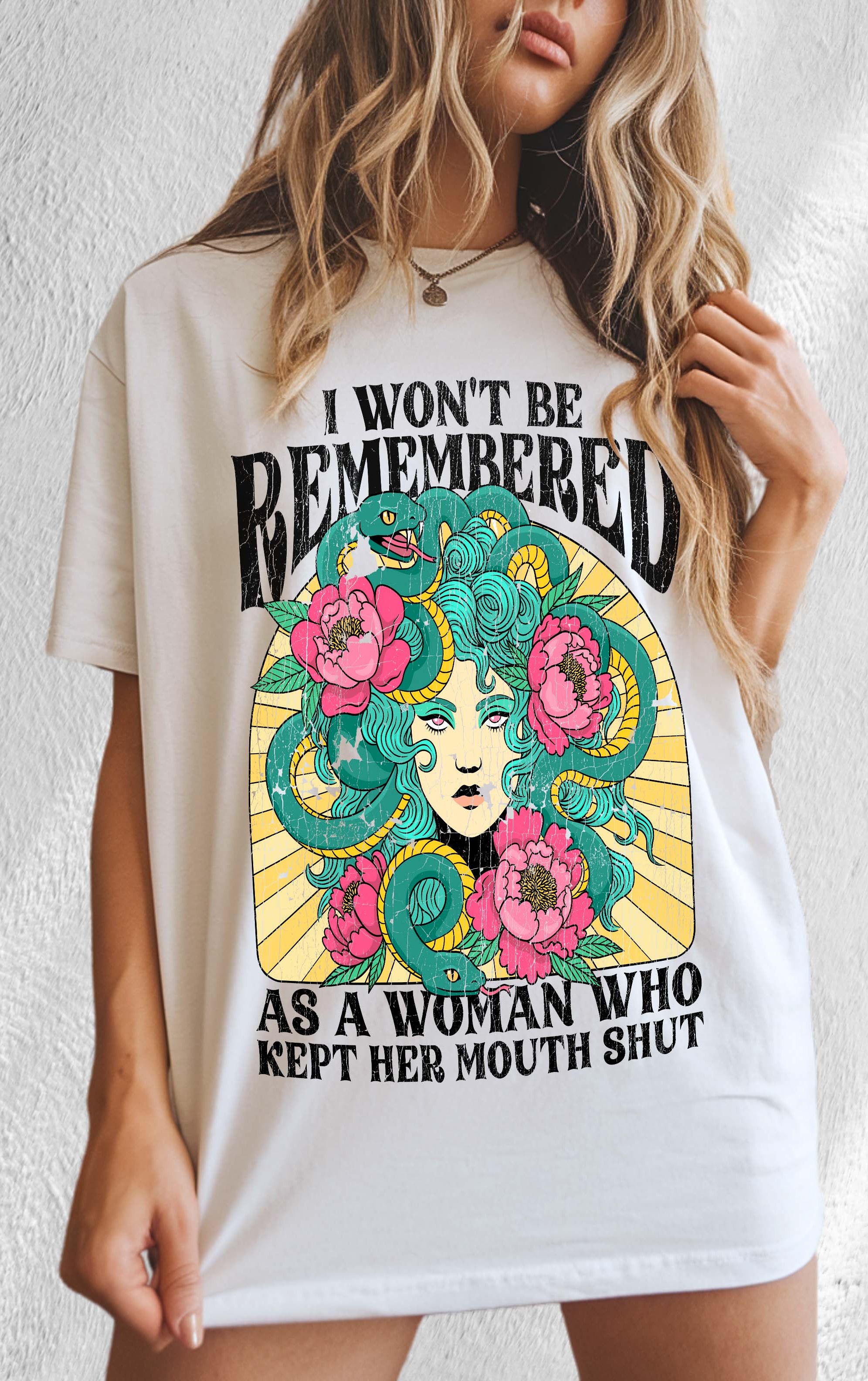 A woman modeling a white crew neck t-shirt with a graphic print in the center that reads 'I Won't Be Remembered As A Woman Who Kept Her Mouth Shut' surrounded by floral designs.