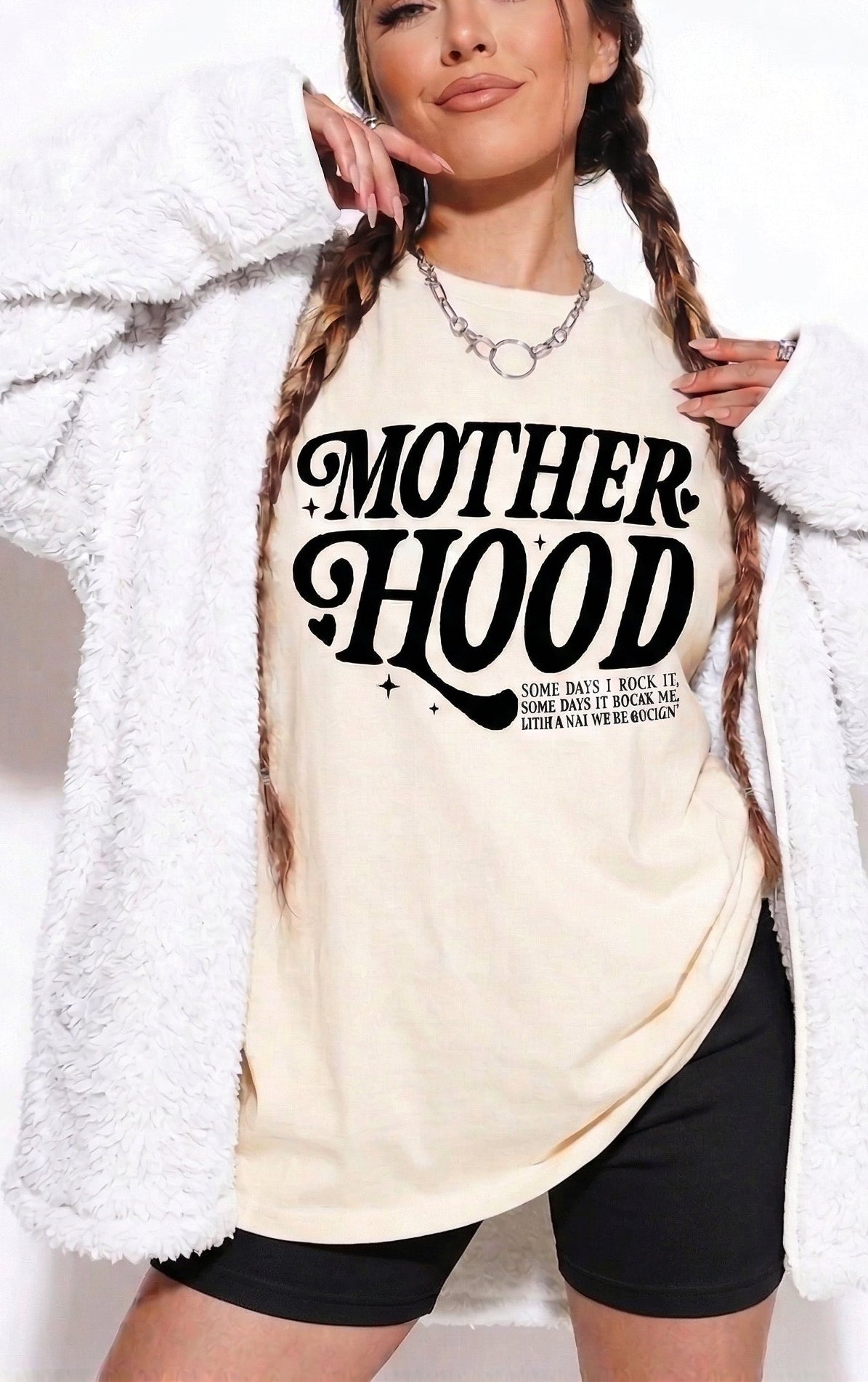 Woman wearing a white t-shirt with 'MOTHERHOOD' text, standing against a plain background