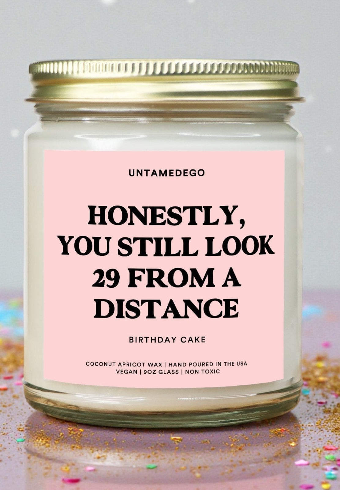 Candle jar with a pink label on a reflective surface with confetti