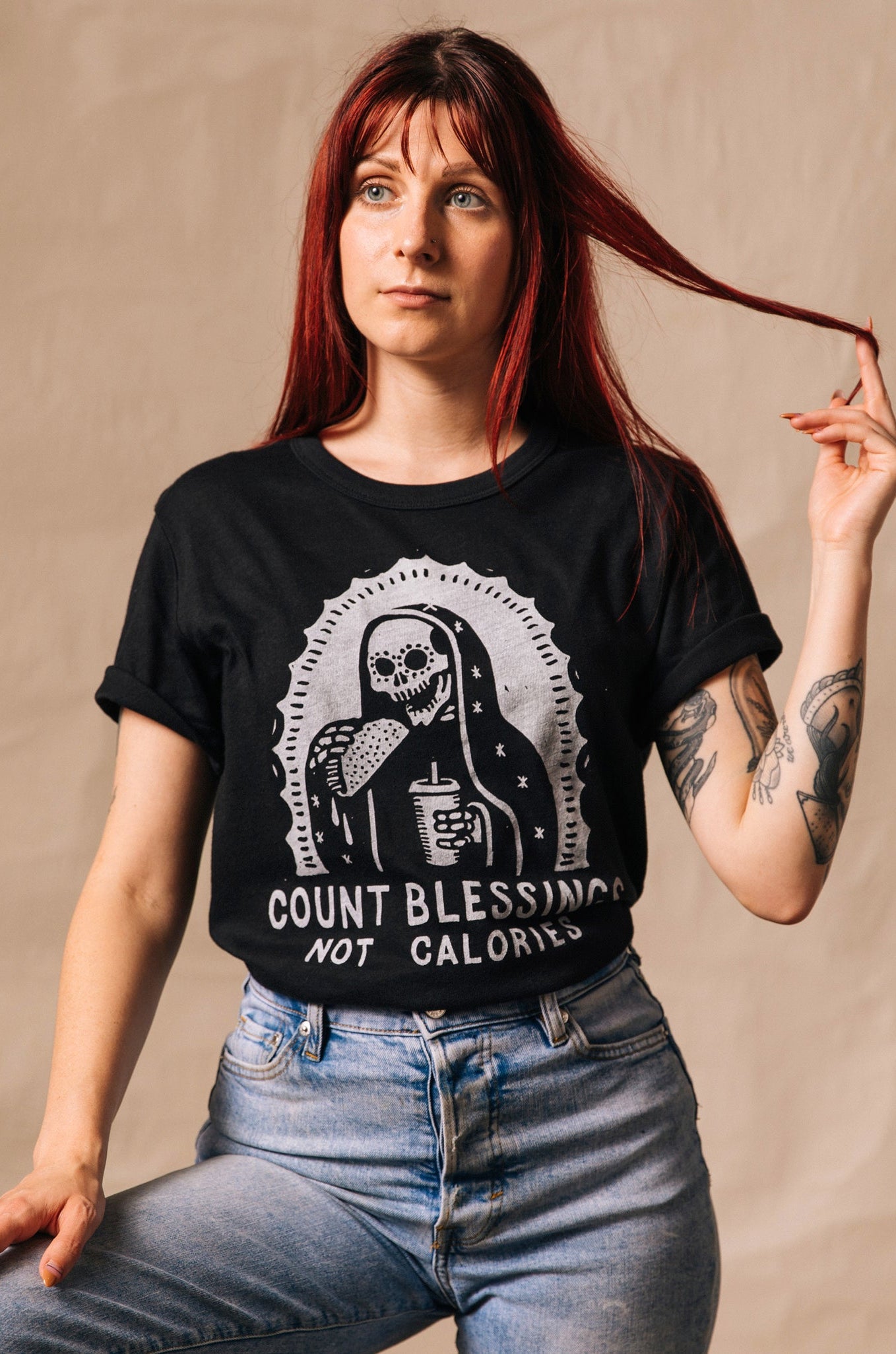 Person wearing a black t-shirt with a graphic design and text, sitting against a beige background