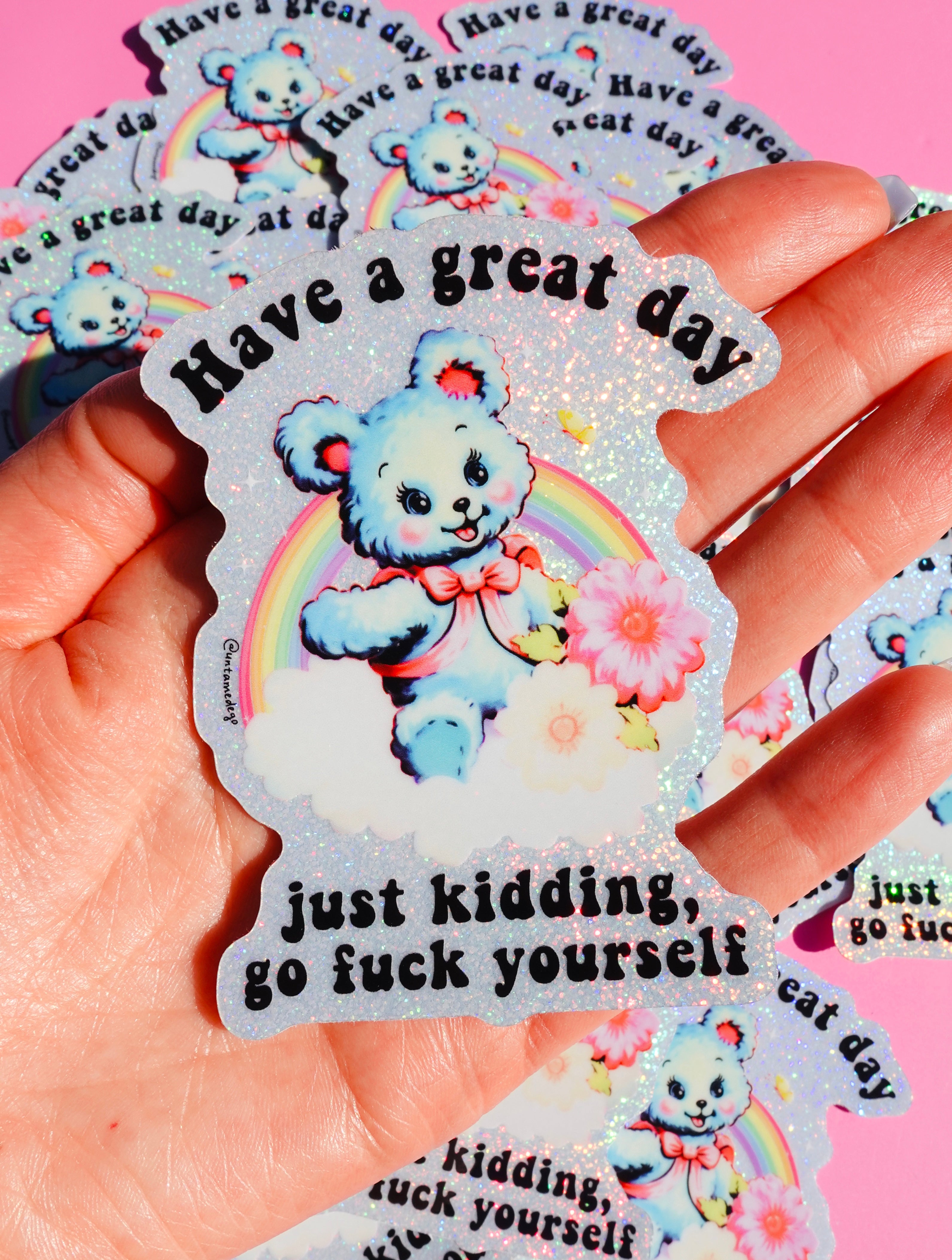 Funny holographic vinyl sticker with pastel blue bear, rainbow, and flowers. Text reads “Have a great day, just kidding, go f*ck yourself.”