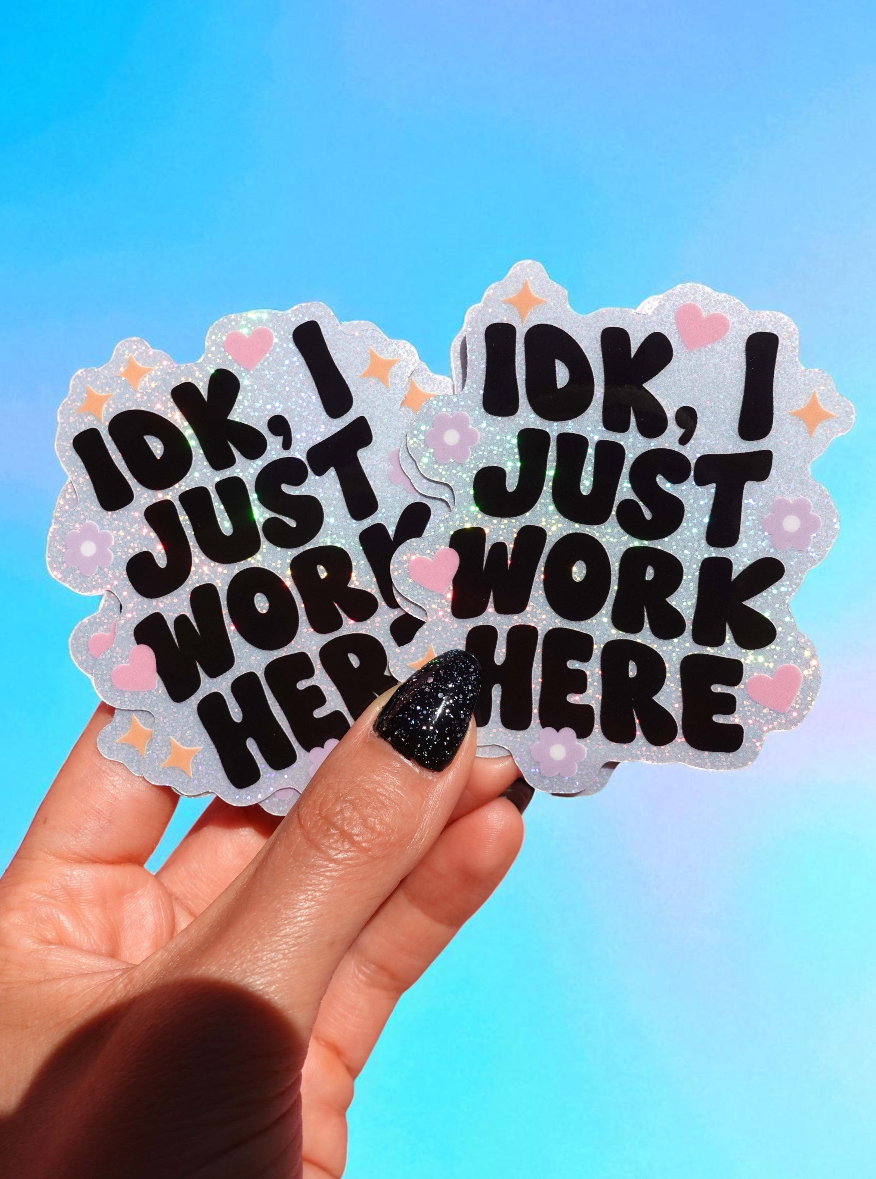 Two stickers with text held by a hand against a colorful gradient background