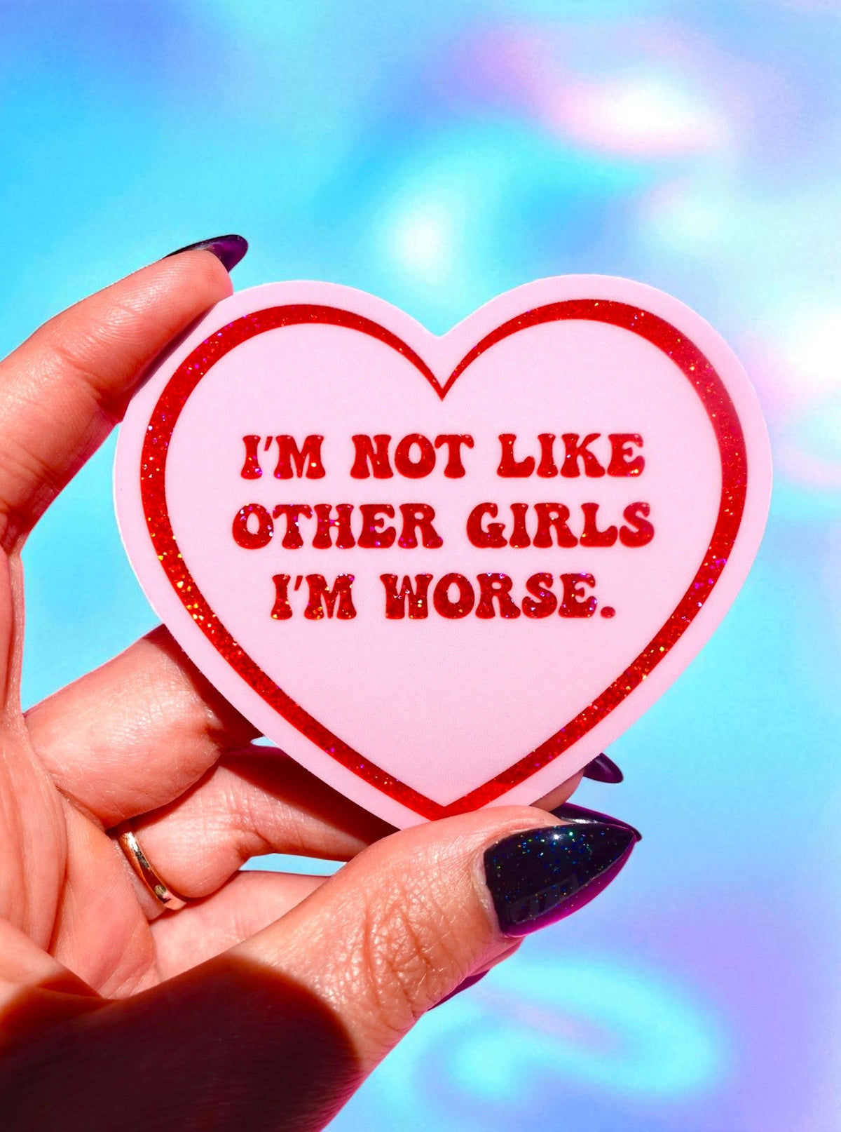 Heart-shaped sticker with text held by a hand against a colorful background