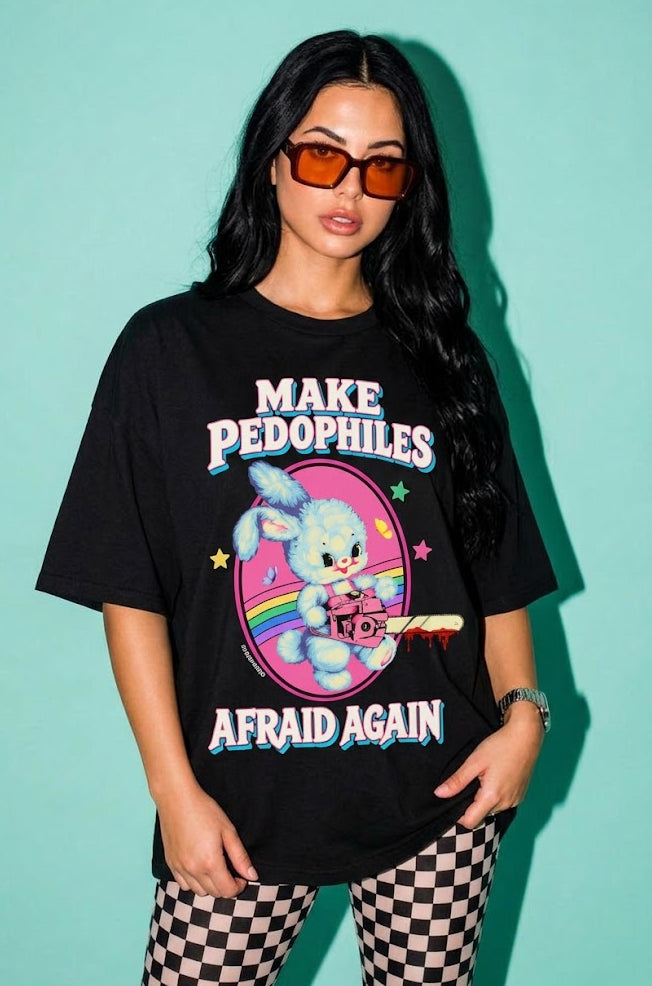 A woman modeling a black graphic t-shirt with the text 'MAKE PEDOPHILES AFRAID AGAIN' and a cartoon bunny illustration, set against a solid teal background.