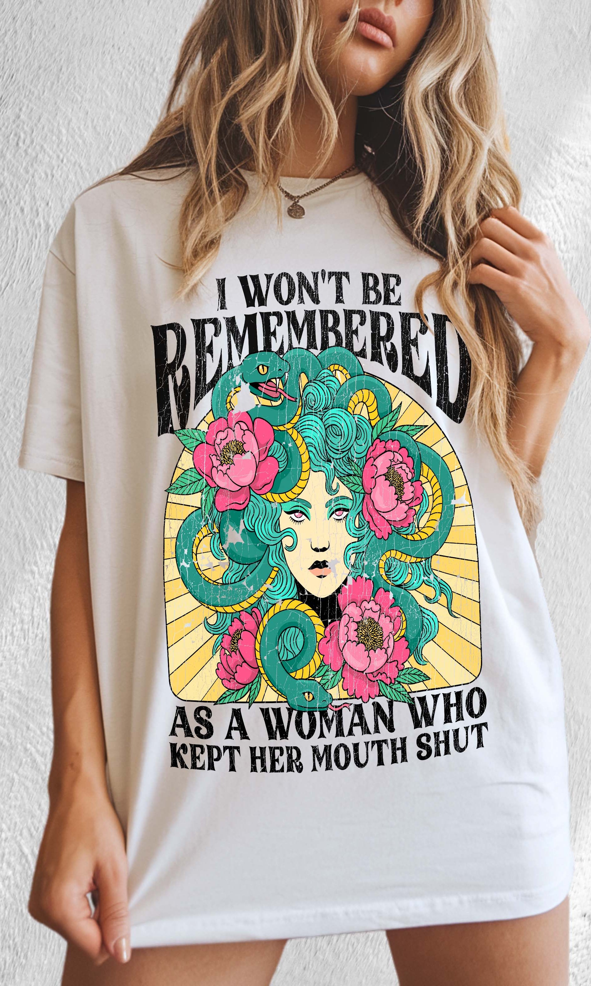A woman modeling a white crew neck t-shirt with a graphic print in the center that reads 'I Won't Be Remembered As A Woman Who Kept Her Mouth Shut' surrounded by floral designs.