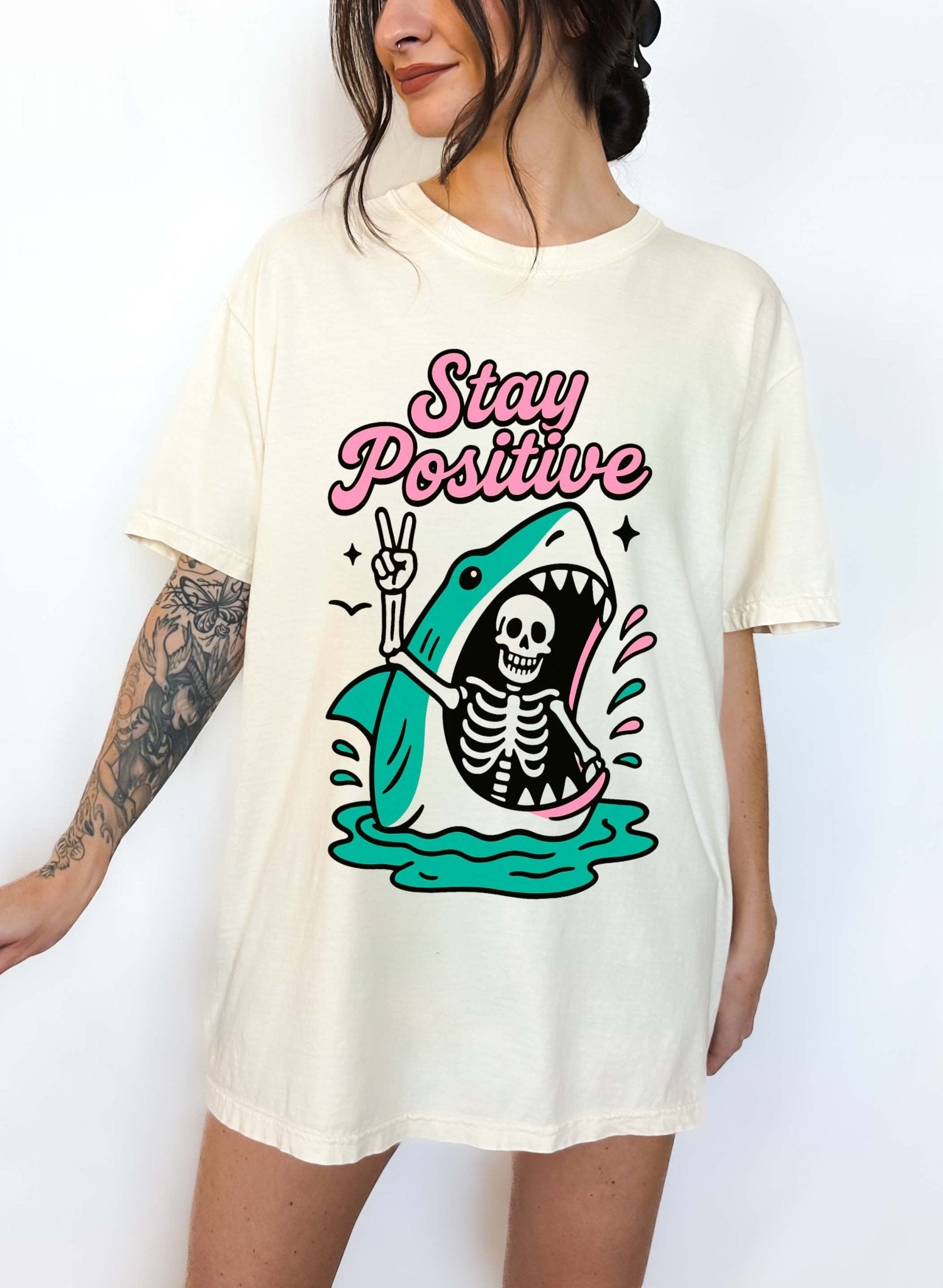 Funny graphic t-shirt with skeleton inside shark illustration and text saying stay positive