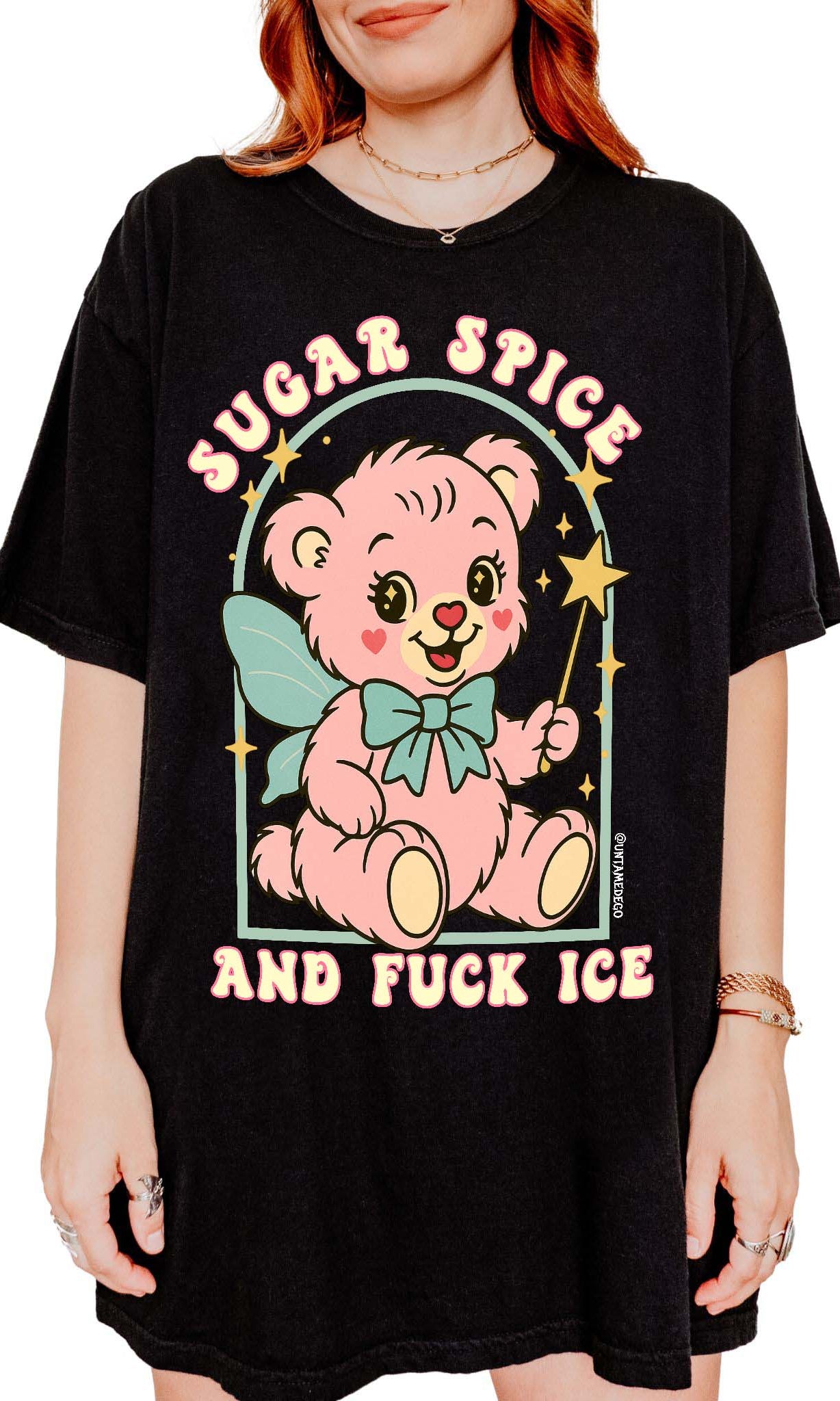 Person wearing a black graphic t-shirt featuring a pastel illustrated bear holding a wand and text that reads Sugar Spice and F star ICE, photographed against a white background