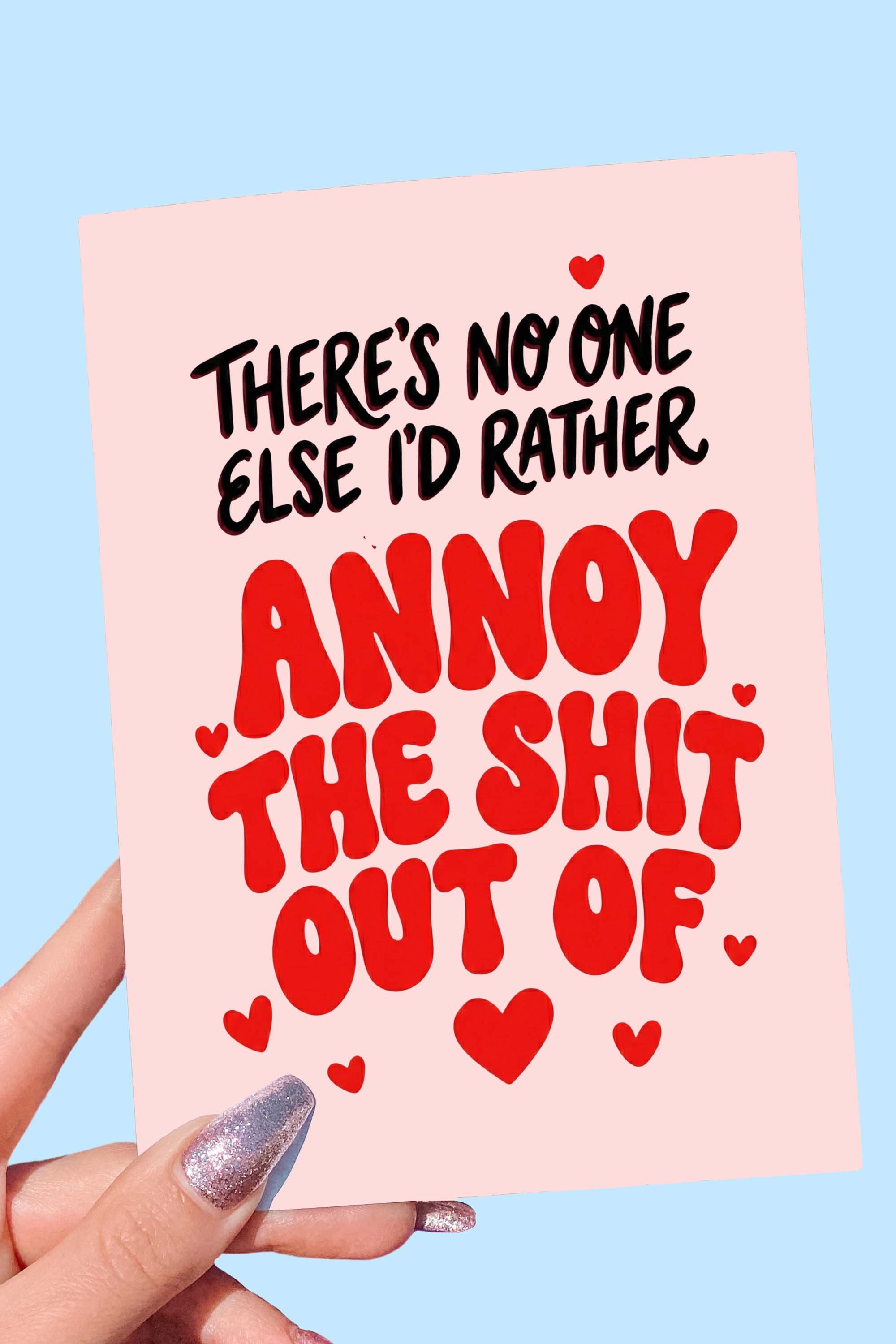 Greeting card with bold red and black text and heart graphics on a pink background, photographed being held by a hand