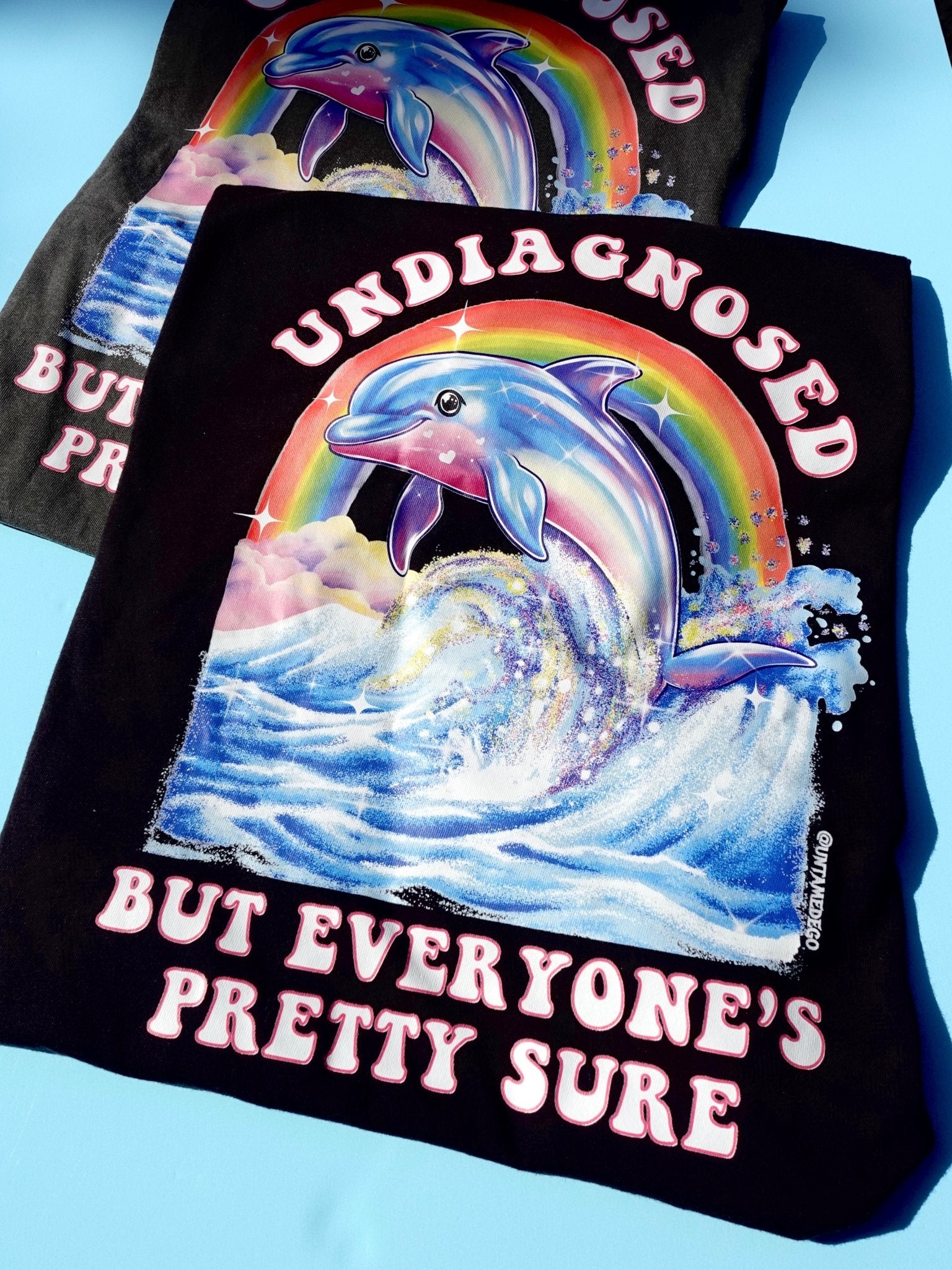 Funny graphic t-shirt with dolphin and rainbow design and text saying undiagnosed but everyone’s pretty sure
