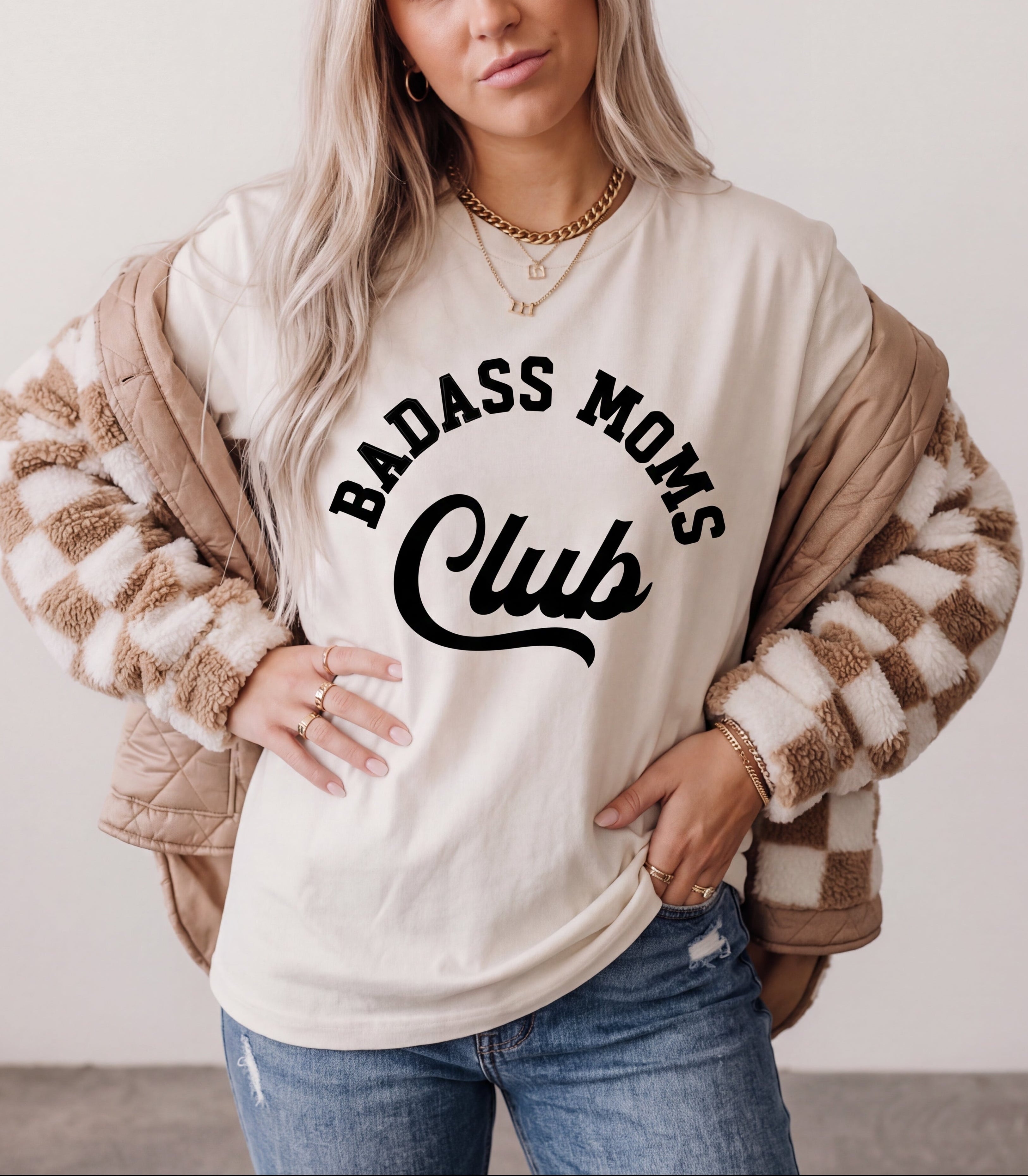 Woman wearing a white sweatshirt with 'Baddass Moms Club' text, standing against a plain background.