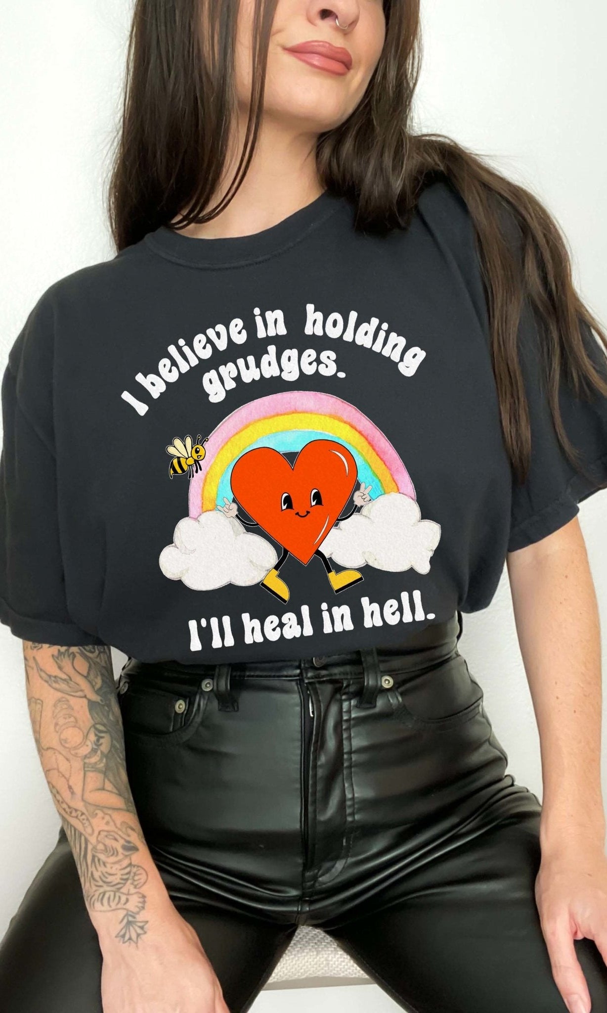Funny sarcastic black t-shirt with retro heart and rainbow graphic reading I believe in holding grudges I’ll heal in hell