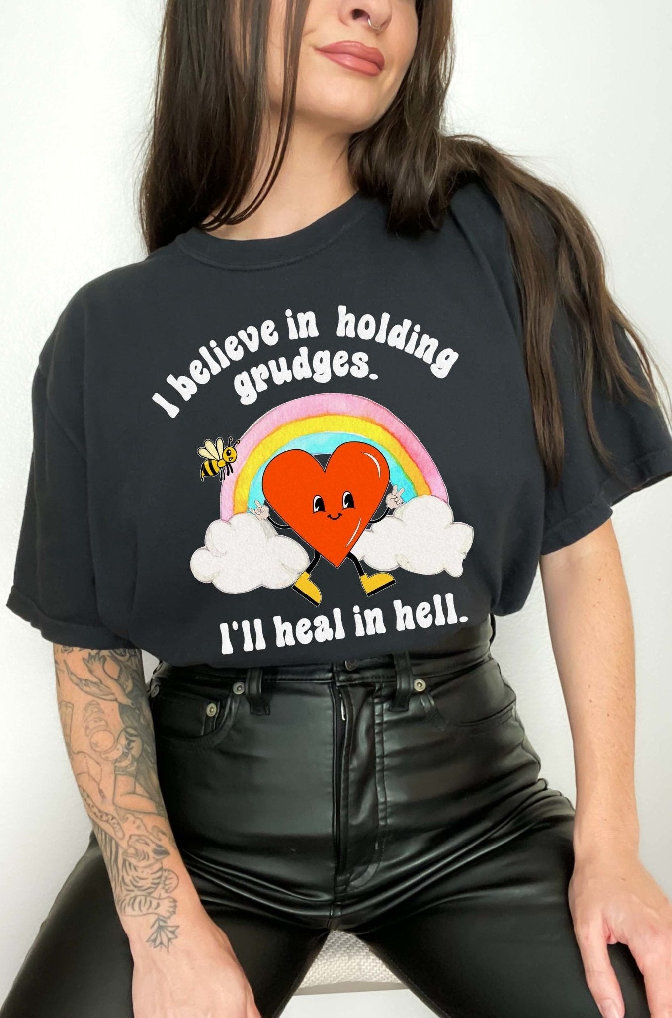 Funny sarcastic black t-shirt with retro heart and rainbow graphic reading I believe in holding grudges I’ll heal in hell