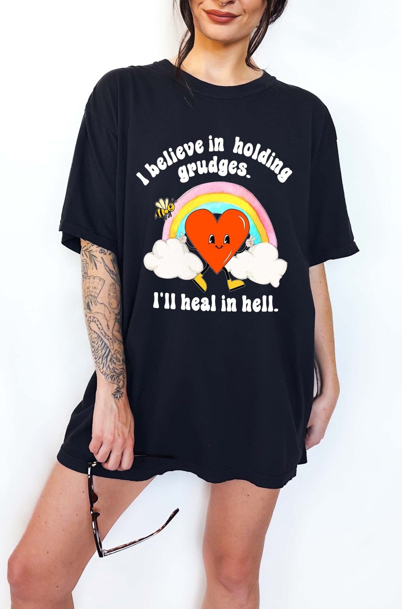 Funny sarcastic black t-shirt with retro heart and rainbow graphic reading I believe in holding grudges I’ll heal in hell