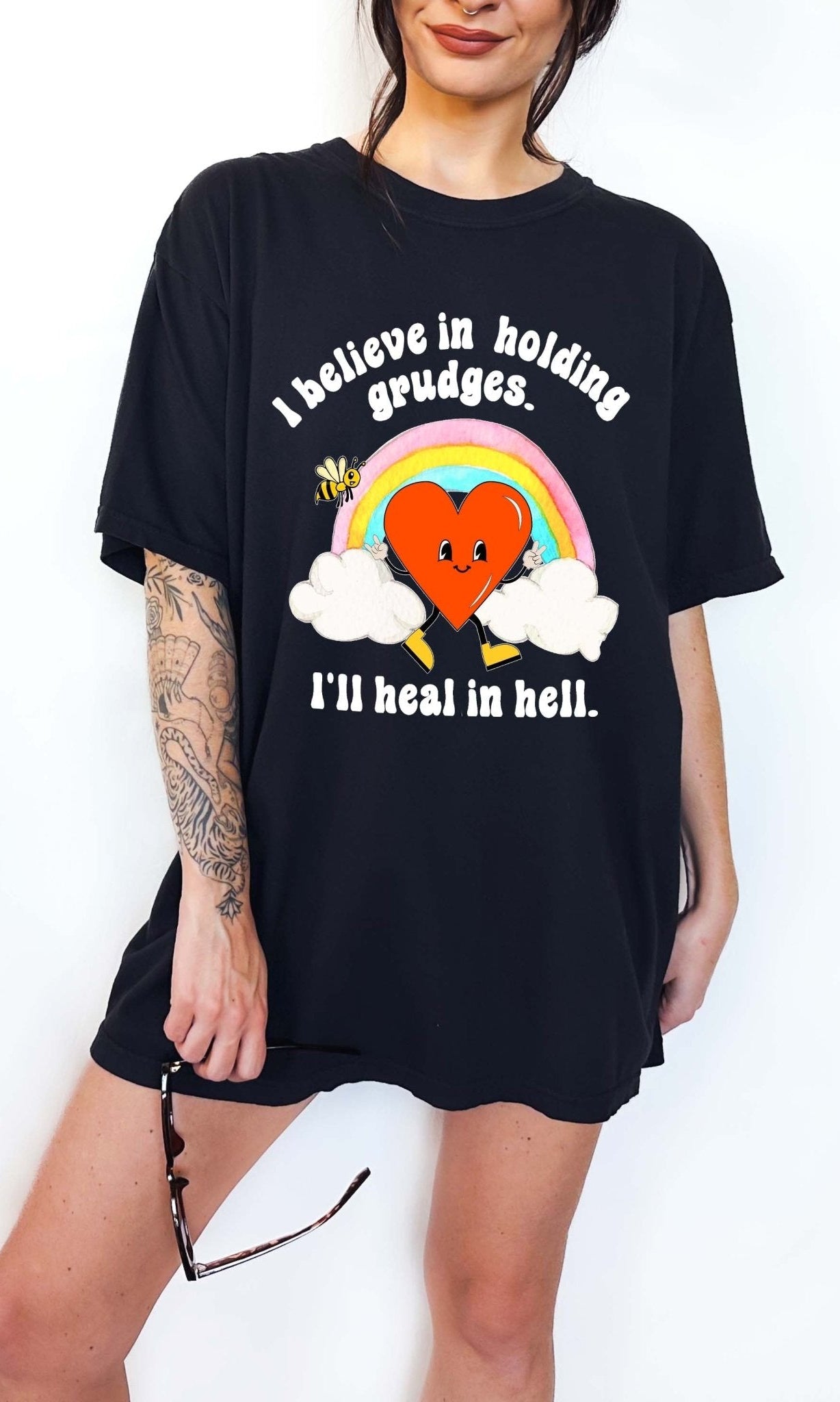 Funny sarcastic black t-shirt with retro heart and rainbow graphic reading I believe in holding grudges I’ll heal in hell