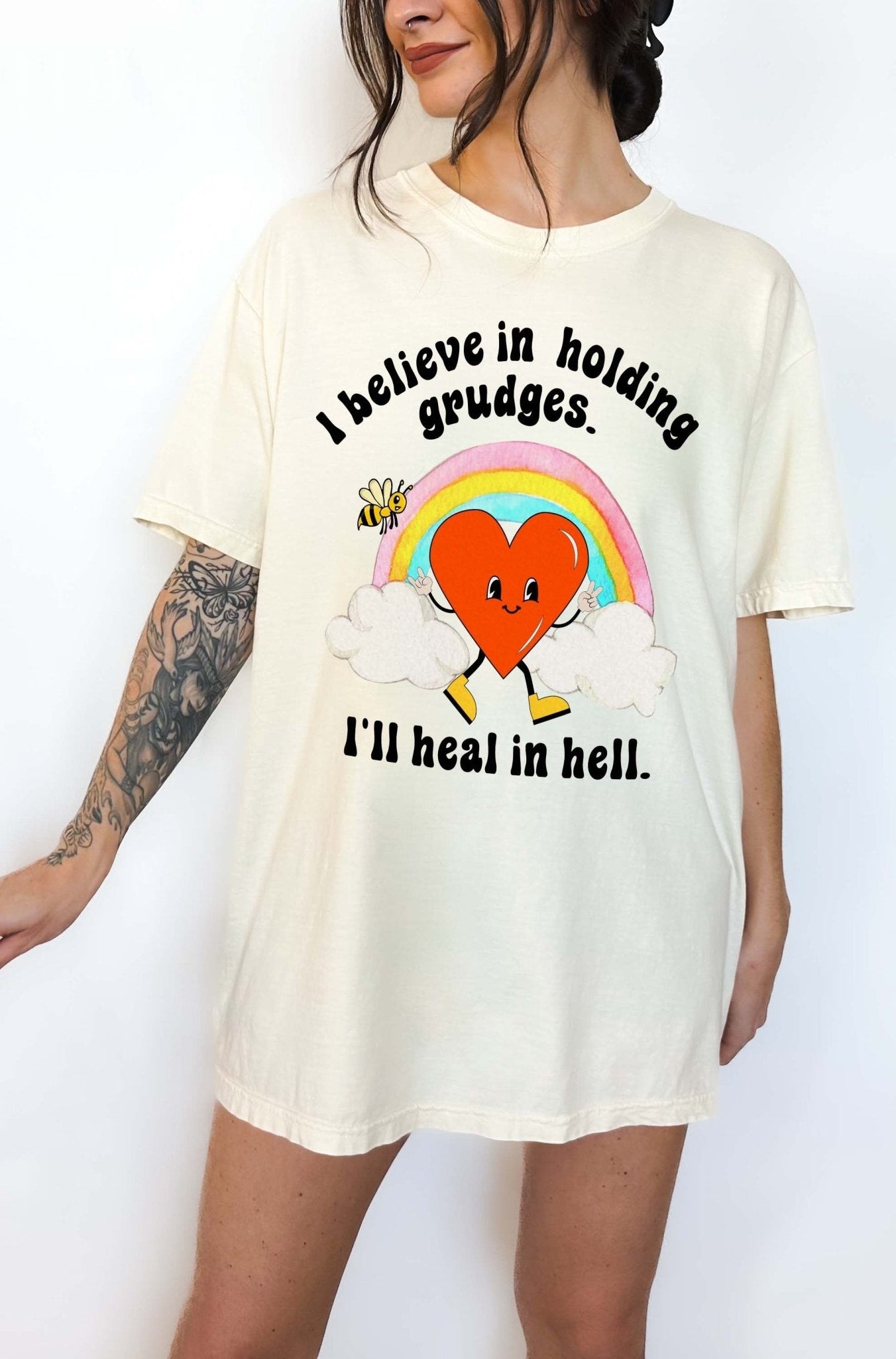 Funny sarcastic black t-shirt with retro heart and rainbow graphic reading I believe in holding grudges I’ll heal in hell