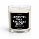 A clear glass jar candle with cream-colored wax and a black label that reads 'DUMPSTER FIRE RESPONSE TEAM' in white text, photographed on a clean white background.