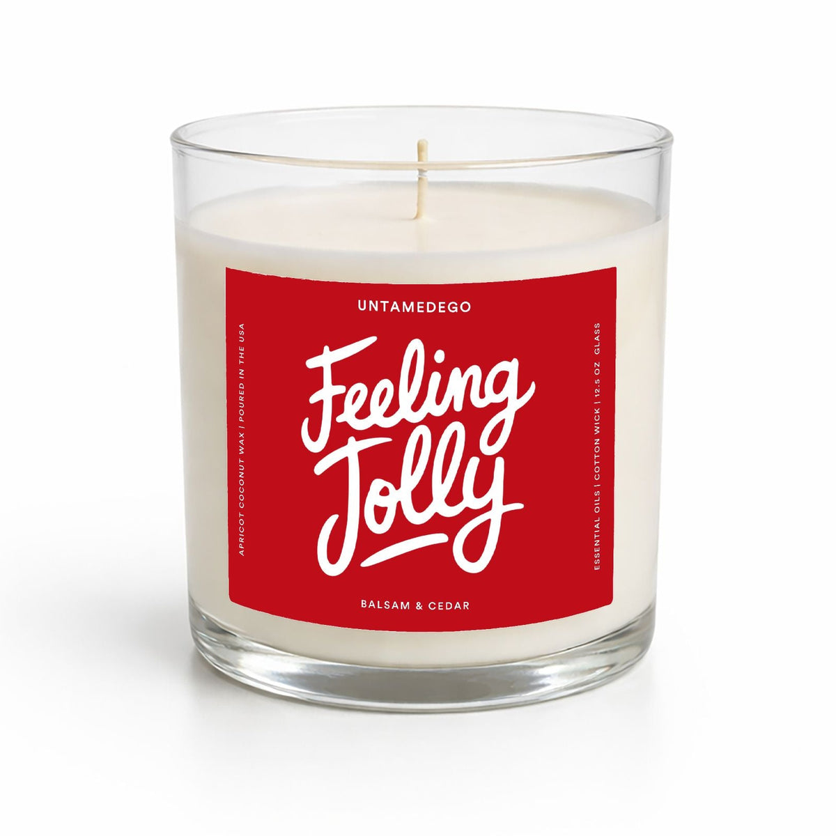 A clear glass jar candle with white wax and a red label reading 'Feeling Jolly' in white script, photographed on a clean white background.