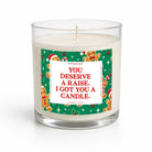 A clear glass jar candle with white wax and a single wick, featuring a festive green holiday label with gingerbread illustrations and the text 'YOU DESERVE A RAISE, I GOT YOU A CANDLE.' on a white background.