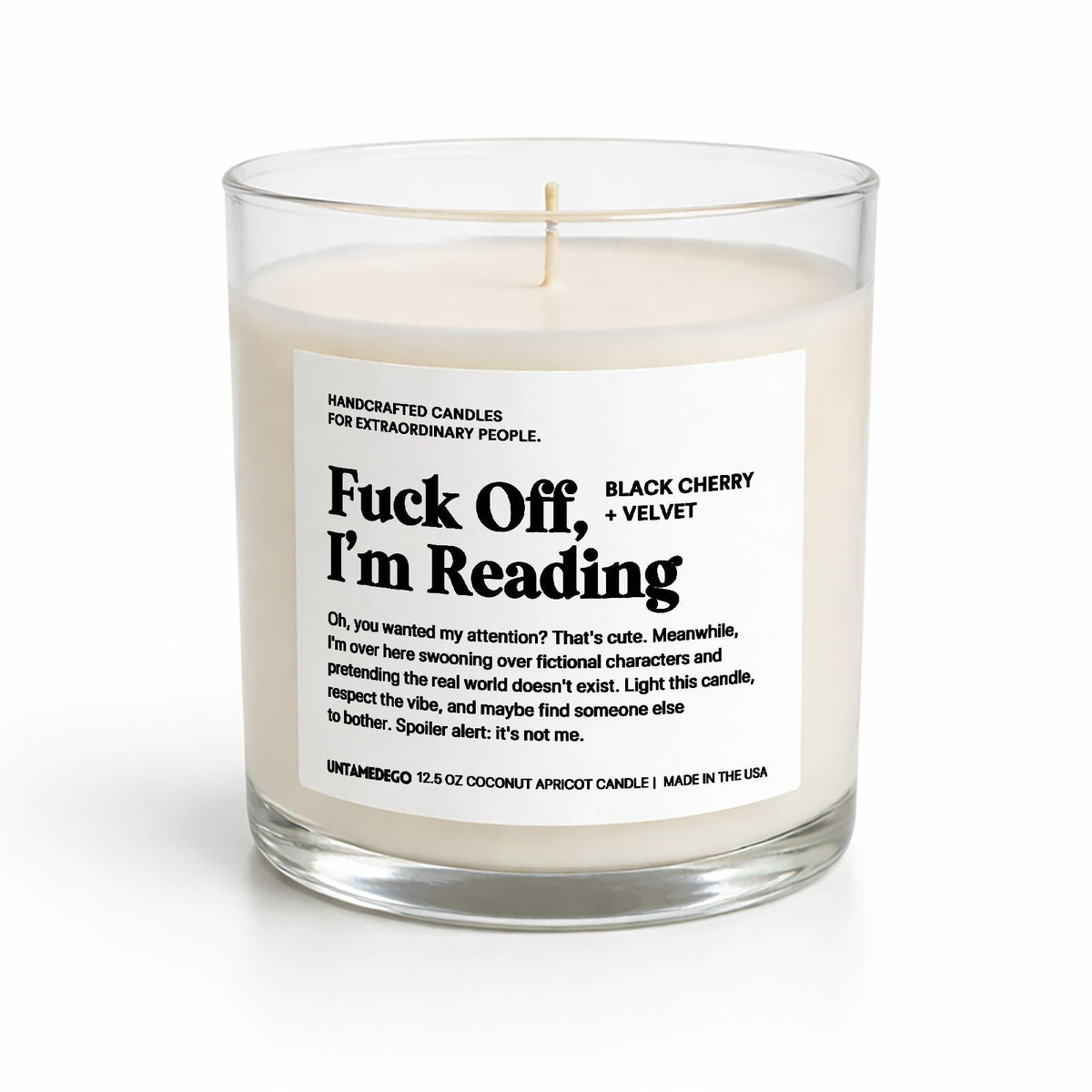 A 12 oz coconut apricot candle in a clear glass jar with a white label that reads 'Fuck Off, I'm Reading'.