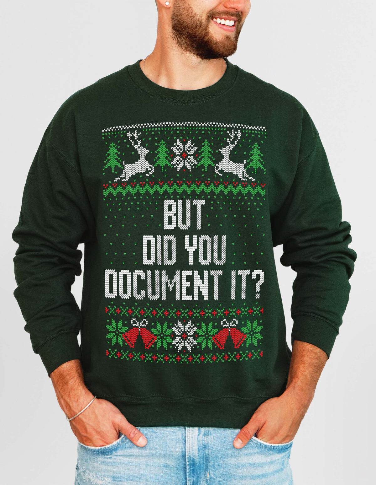 A man wearing a dark green crewneck sweatshirt with a festive Christmas sweater graphic that reads 'BUT DID YOU DOCUMENT IT?' in white text, paired with light blue jeans against a light gray background.