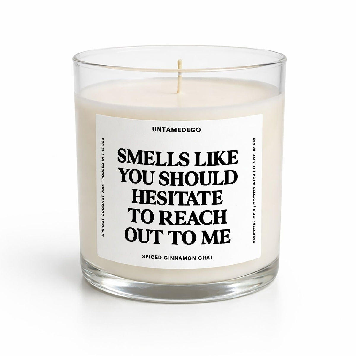 A clear glass jar candle with white wax and a white label featuring bold black text that reads, 'SMELLS LIKE YOU SHOULD HESITATE TO REACH OUT TO ME.' The brand name 'UNTAMEDGO' is visible at the top of the label.