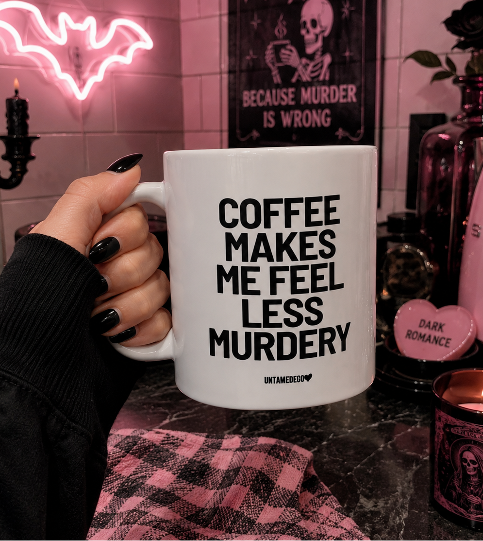 A hand with black nail polish holds a white ceramic mug printed with the text 'COFFEE MAKES ME FEEL LESS MURDERY' and 'UNETHICALGAY'. The background is a dimly lit, gothic-themed room with pink ambient lighting, a pink Smeg kitchen appliance, a pink heart-shaped candle, and a pink plaid cloth.