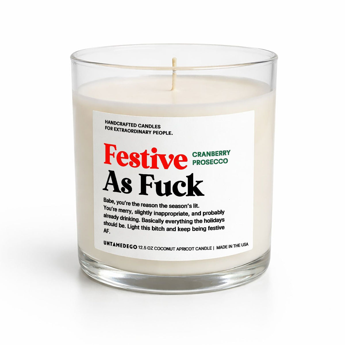A handcrafted soy candle in a clear glass jar with a white label that reads 'Festive As Fuck' in red and black text, with 'Cranberry Prosecco' in green. The candle is photographed on a clean white background.