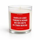 A white wax candle in a clear glass jar with a red front label that reads 'SMELLS LIKE THERE'S SOME HO HO HO'S IN THIS HOUSE' and smaller text 'UNTAMEDEGO' and 'CRANBERRY PROSECCO'.