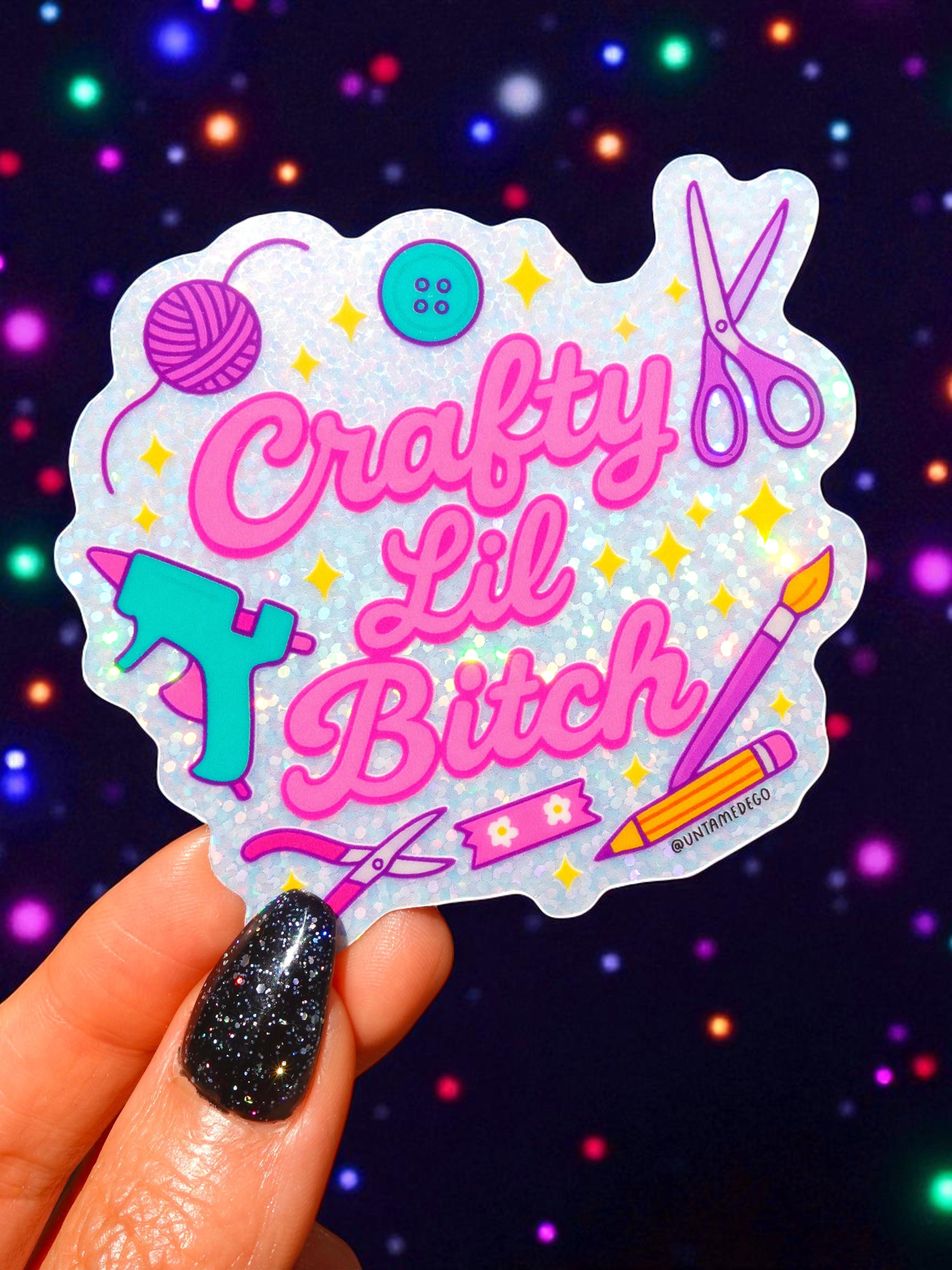 Sticker with 'Crafty Lil Bitch' text held by a hand against a colorful, starry background.
