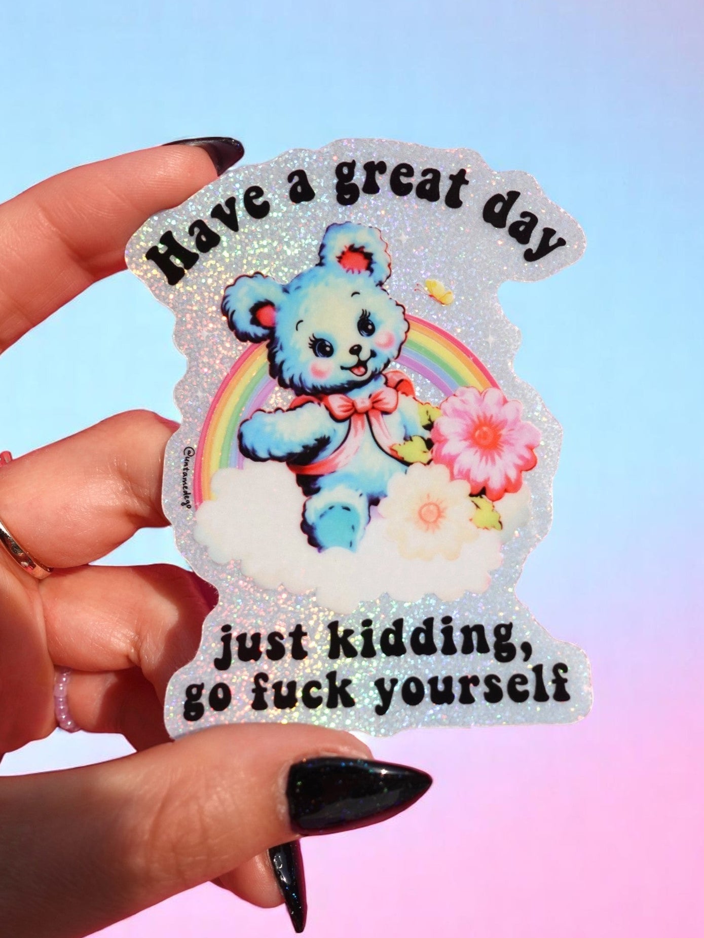 Funny holographic vinyl sticker with pastel blue bear, rainbow, and flowers. Text reads “Have a great day, just kidding, go f*ck yourself.”