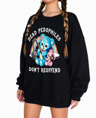 A person wearing an oversized black sweatshirt with a large graphic print featuring a blue teddy bear, a pink teddy bear, a rainbow, and the text 'DEAD PEDOPHILES DON'T REOFFEND' on a plain white background.