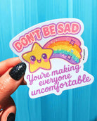 Sticker with a rainbow and star design held by a hand against a blue background