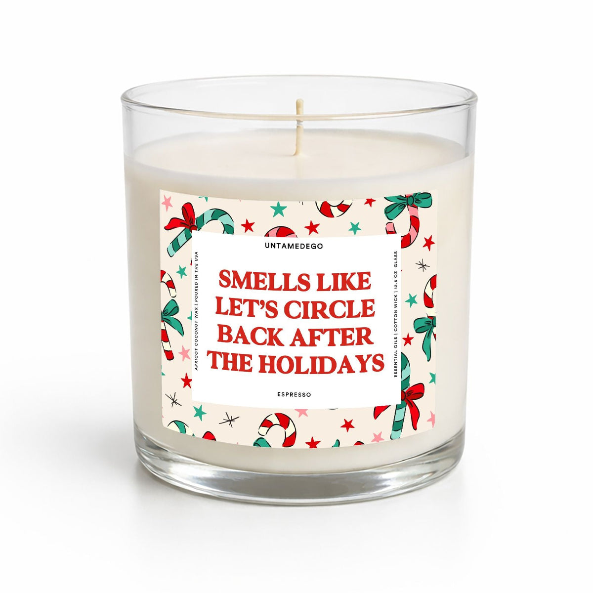 A clear glass jar candle with white wax and a humorous holiday-themed paper label that reads 'SMELLS LIKE LET'S CIRCLE BACK AFTER THE HOLIDAYS' in red text, surrounded by red and green holiday illustrations. The candle is photographed on a clean white background.