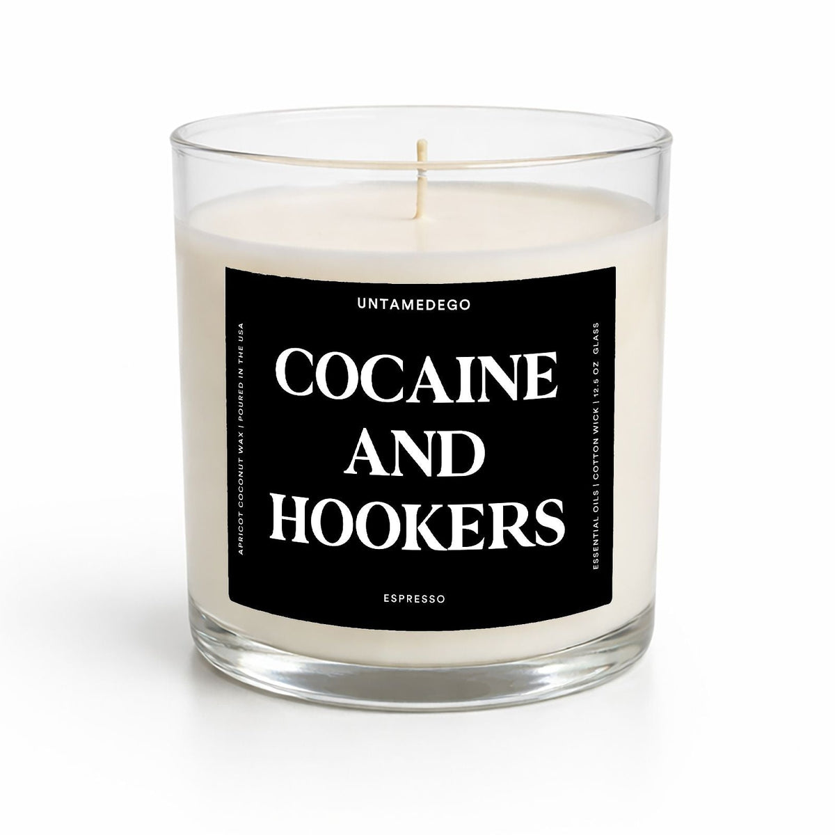 A clear glass jar candle with white wax and a black label reading 'COCAINE AND HOOKERS' in white text, photographed on a clean white background.