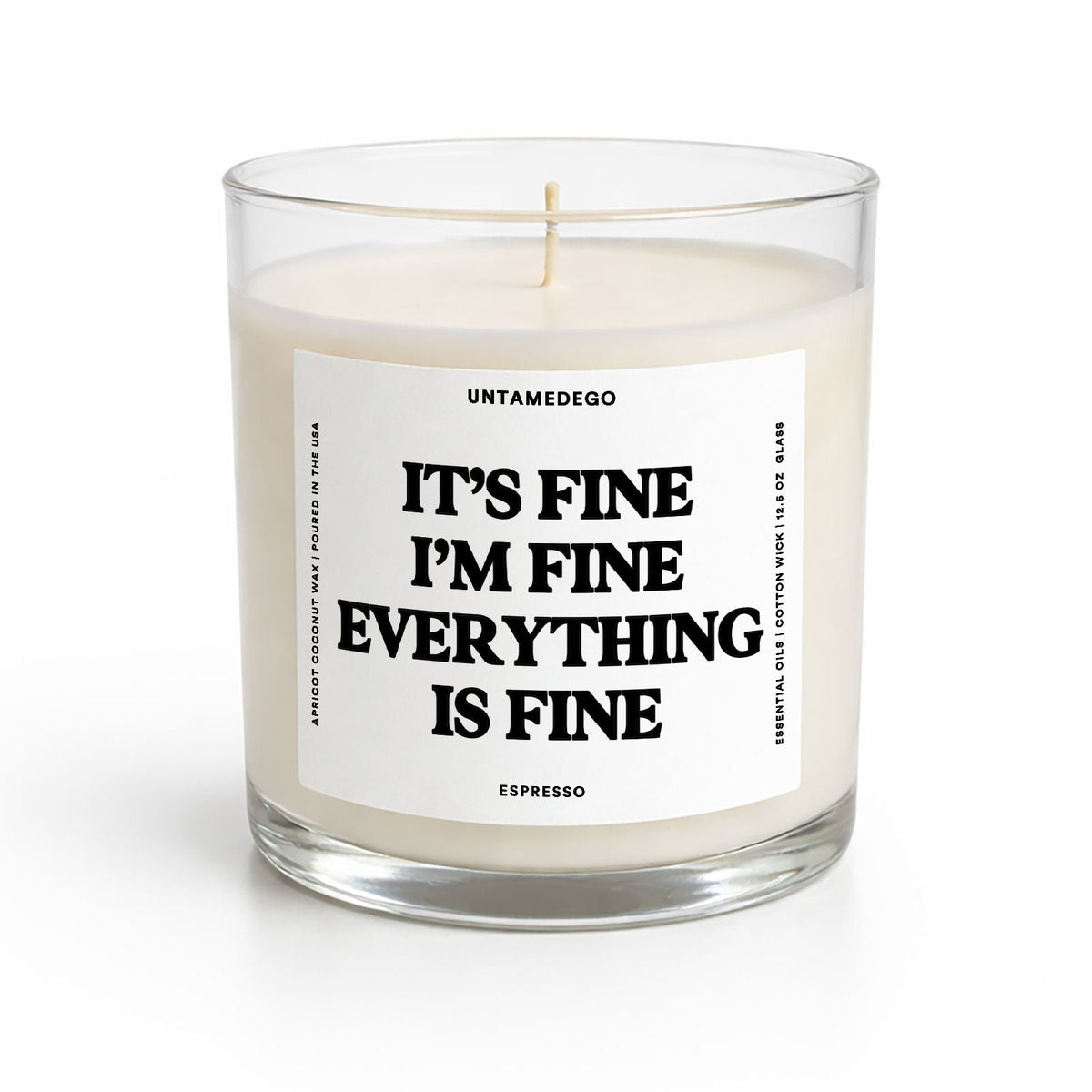 A clear glass jar candle with cream-colored wax and a white label featuring bold black text that reads 'IT'S FINE I'M FINE EVERYTHING IS FINE'. The brand name 'UNTAMEDEGO' is visible at the top of the label, with 'ESPRESSO' at the bottom.
