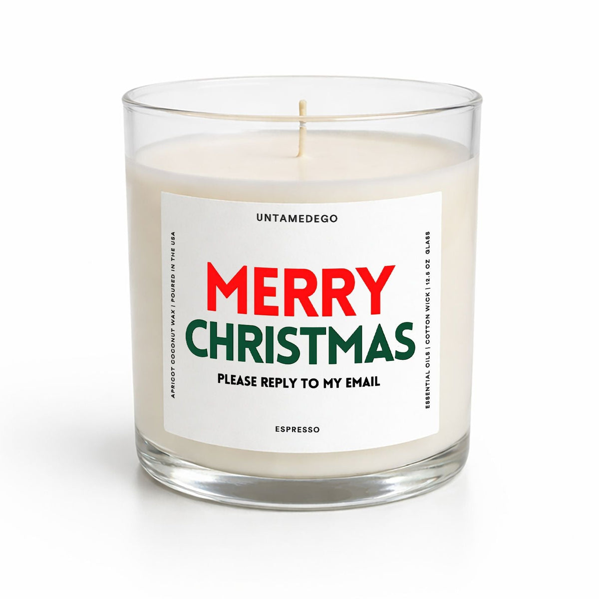 A clear glass jar candle with white wax and a single wick, featuring a white label that reads 'MERRY CHRISTMAS' in red and green text with smaller black text below. The brand name 'UNTAMEDEGO' is visible at the top of the label.