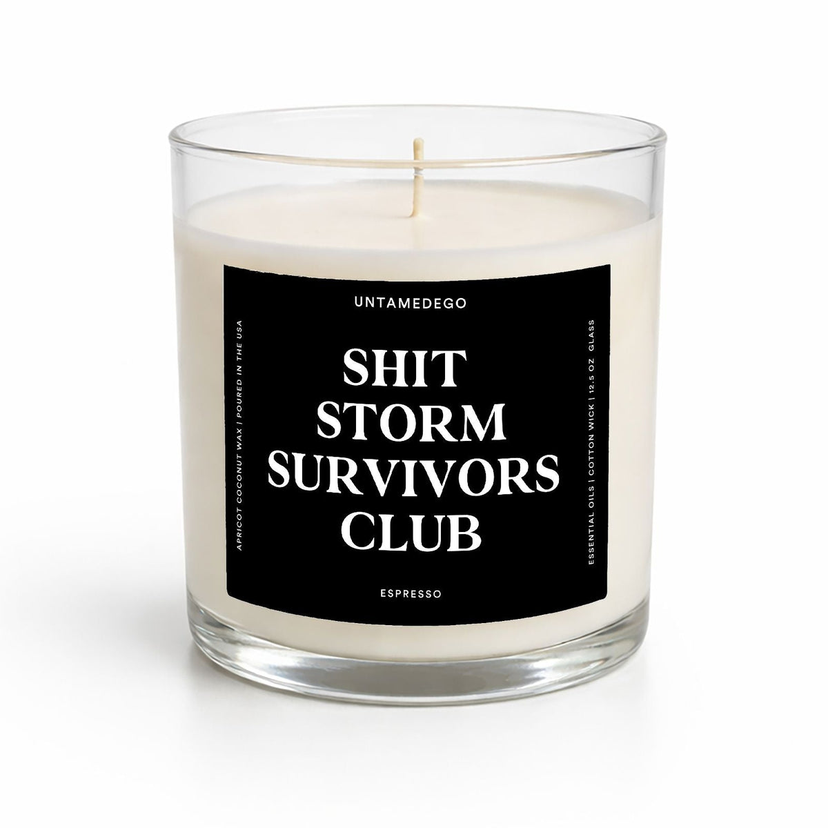 A clear glass jar candle with white wax and a black front label reading 'SHIT STORM SURVIVORS CLUB' in white text. The brand name 'UNTAMEDEGO' is visible at the top of the label.